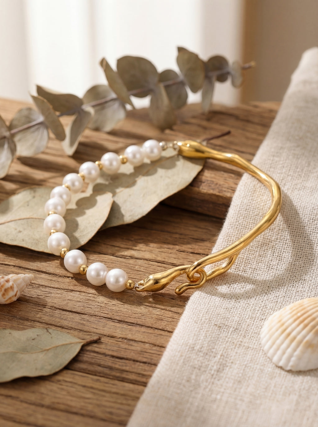 Pearl and gold bracelet on a wooden surface with leaves and shells