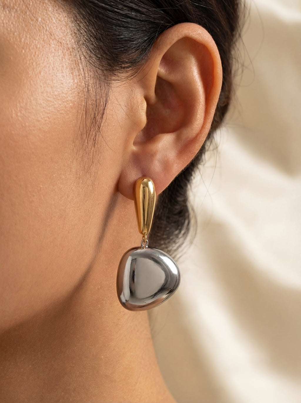 Close-up of an ear wearing a silver heart-shaped earring with gold accents.