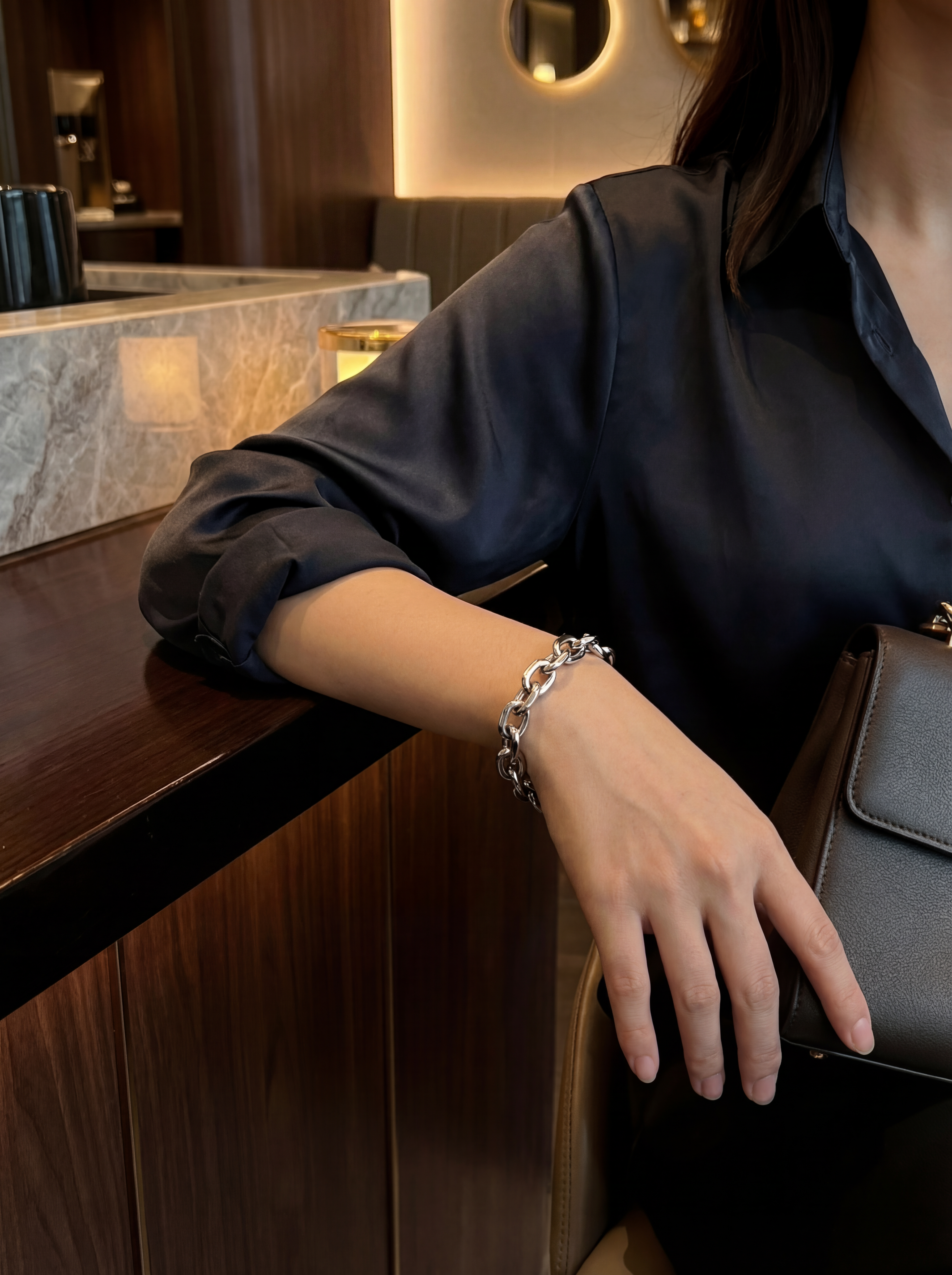 Person wearing a bracelet and holding a black handbag in an indoor setting