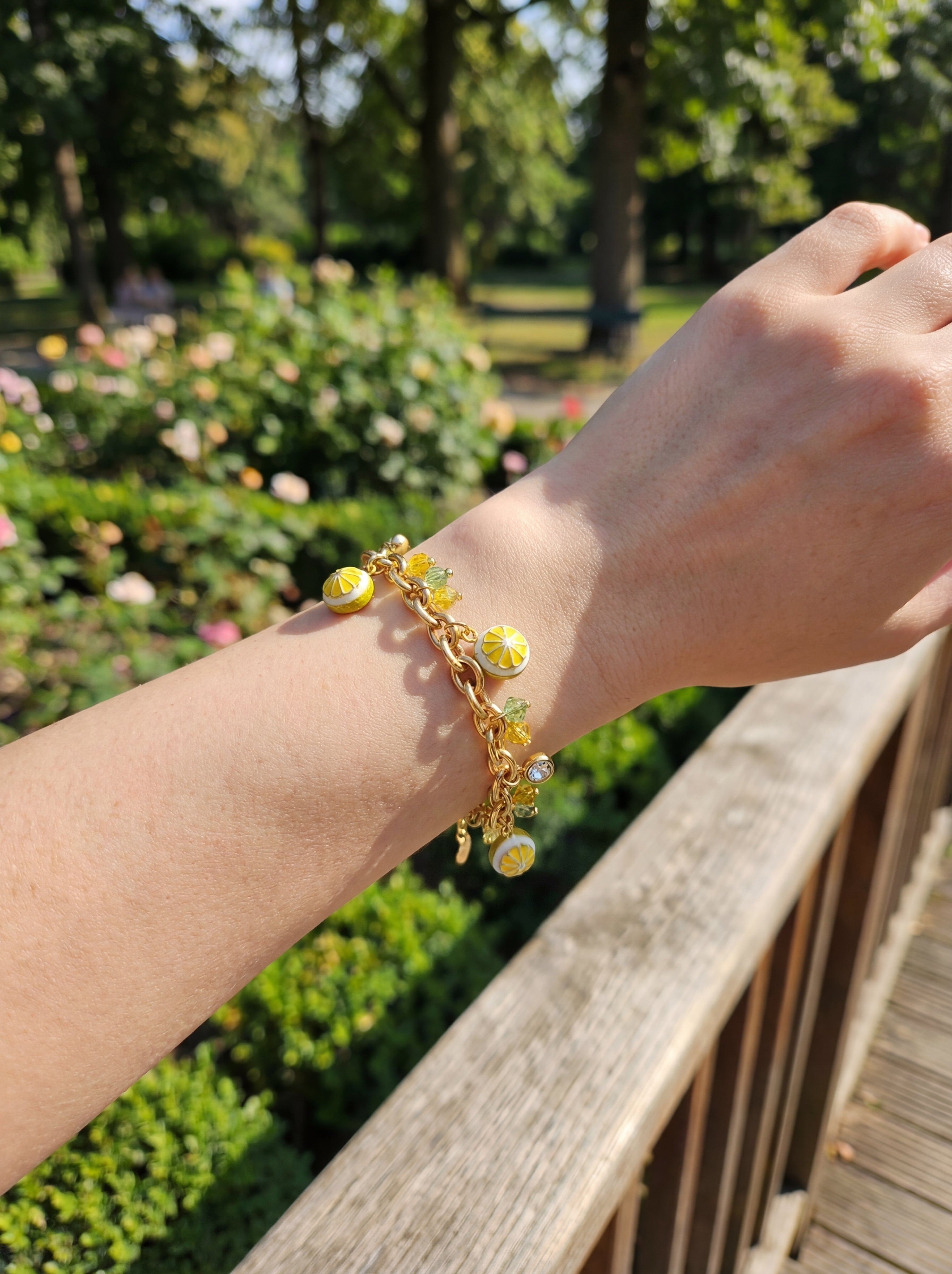 Gold bracelet with yellow charms on a wrist against a blurred garden background