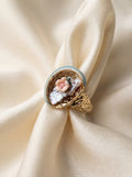 Gold ring with floral design on a beige fabric background