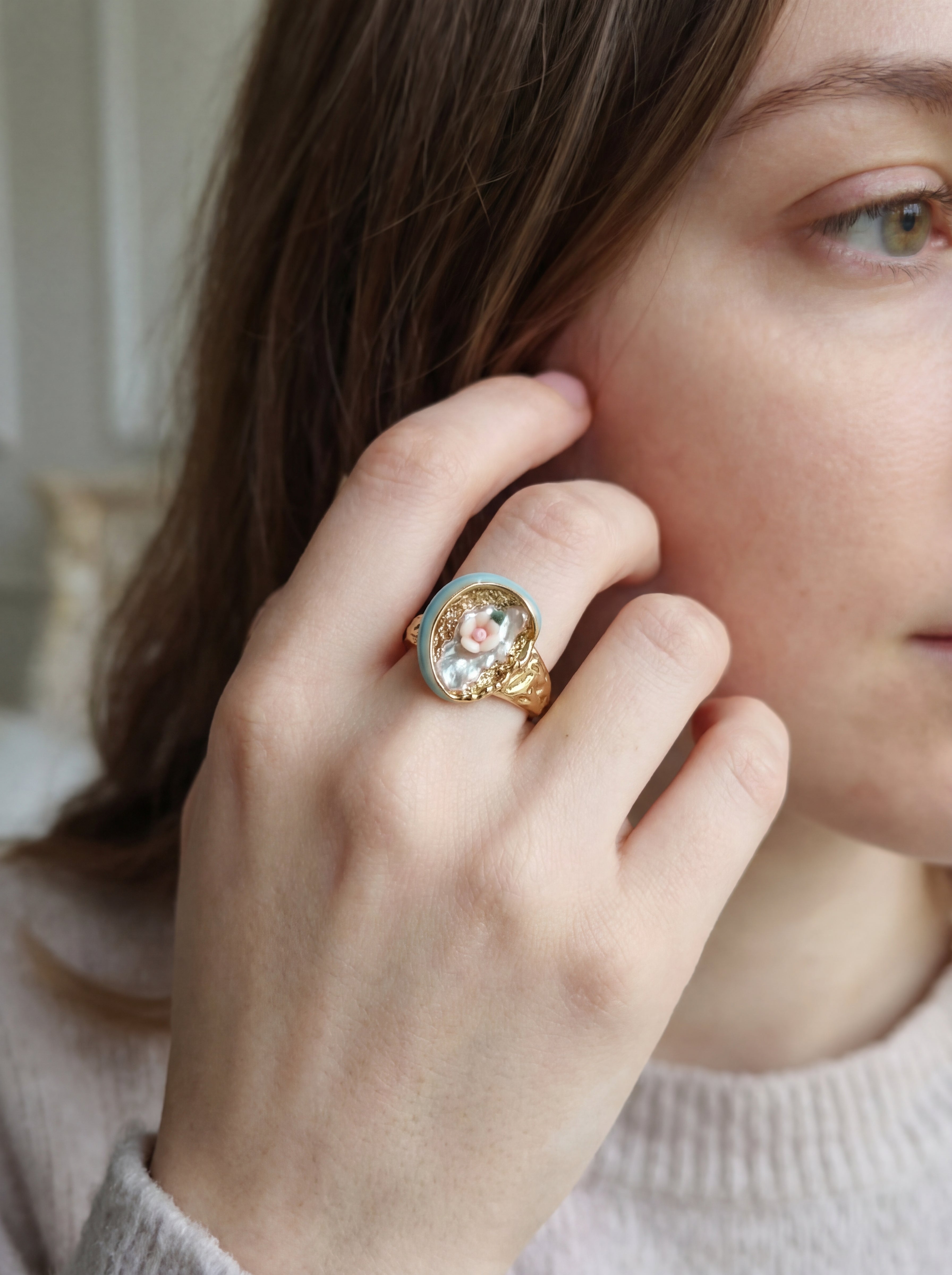 Close-up of a hand wearing a decorative ring with a detailed design, held near the ear.