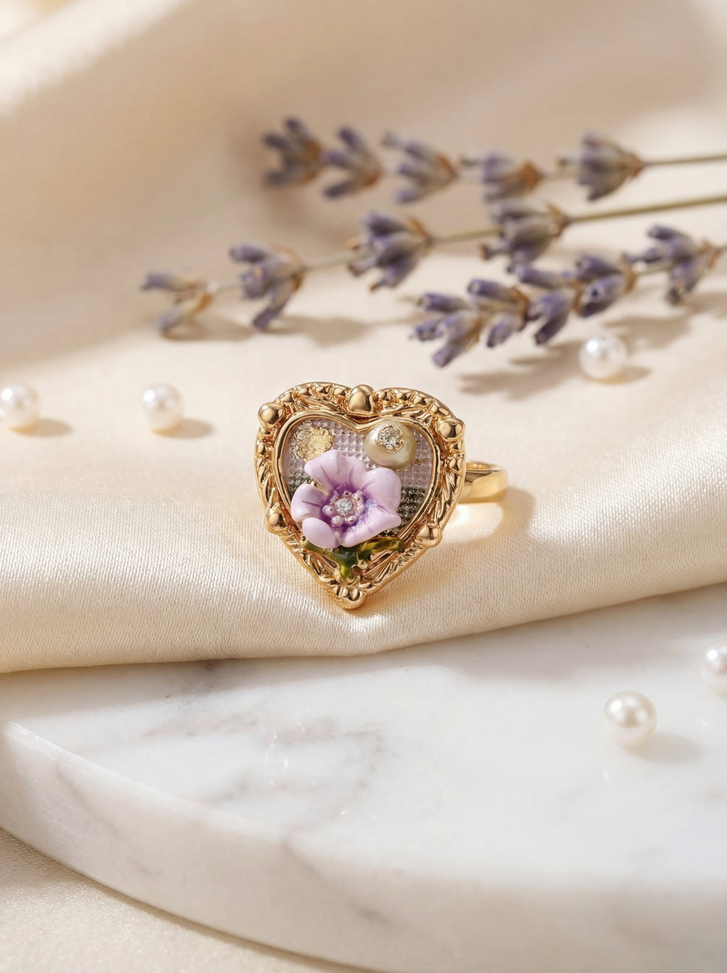 Heart-shaped gold ring with a purple flower and pearl on a soft beige background with lavender flowers.