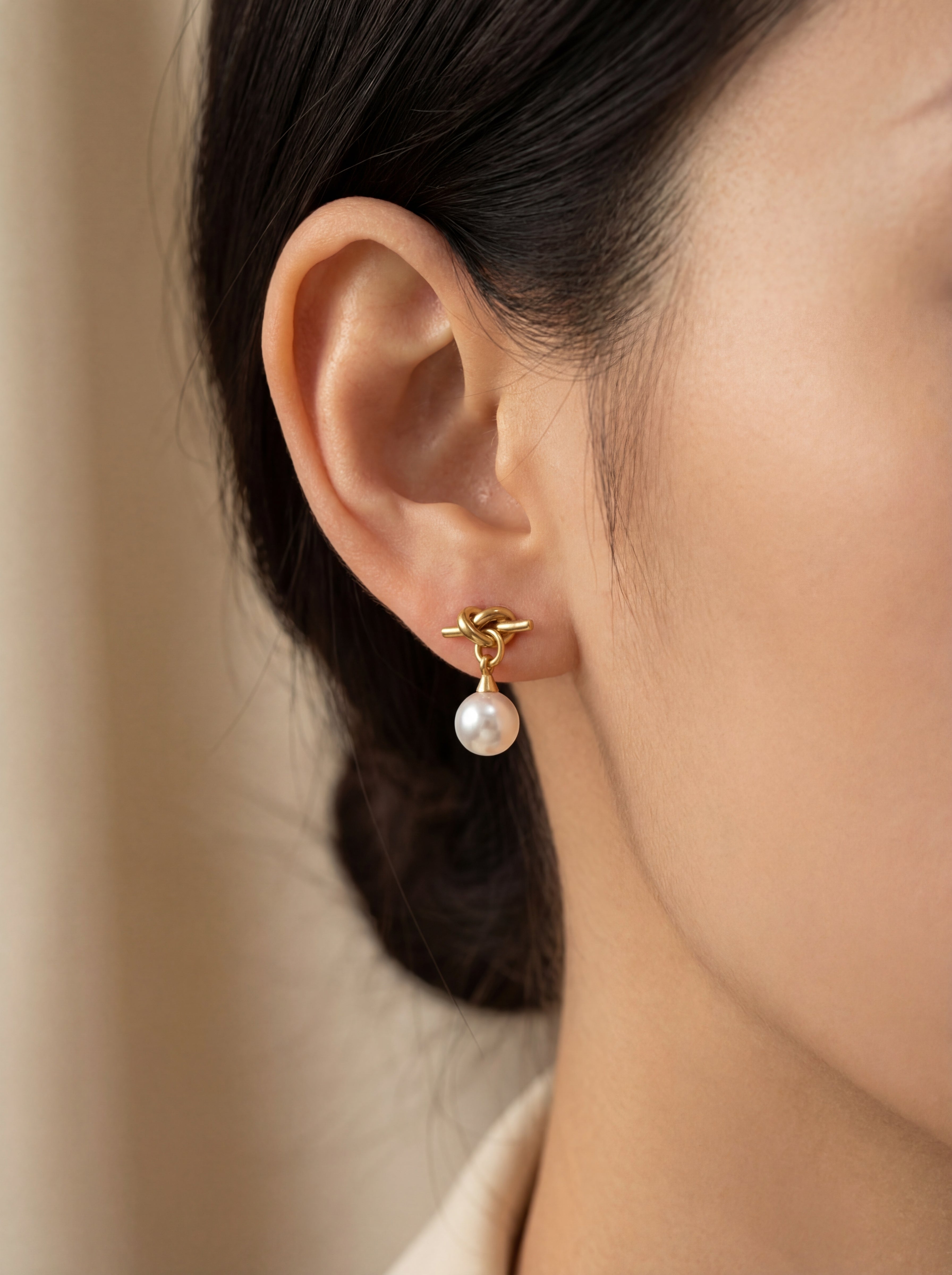 Close-up of an ear wearing a pearl earring with a neutral background