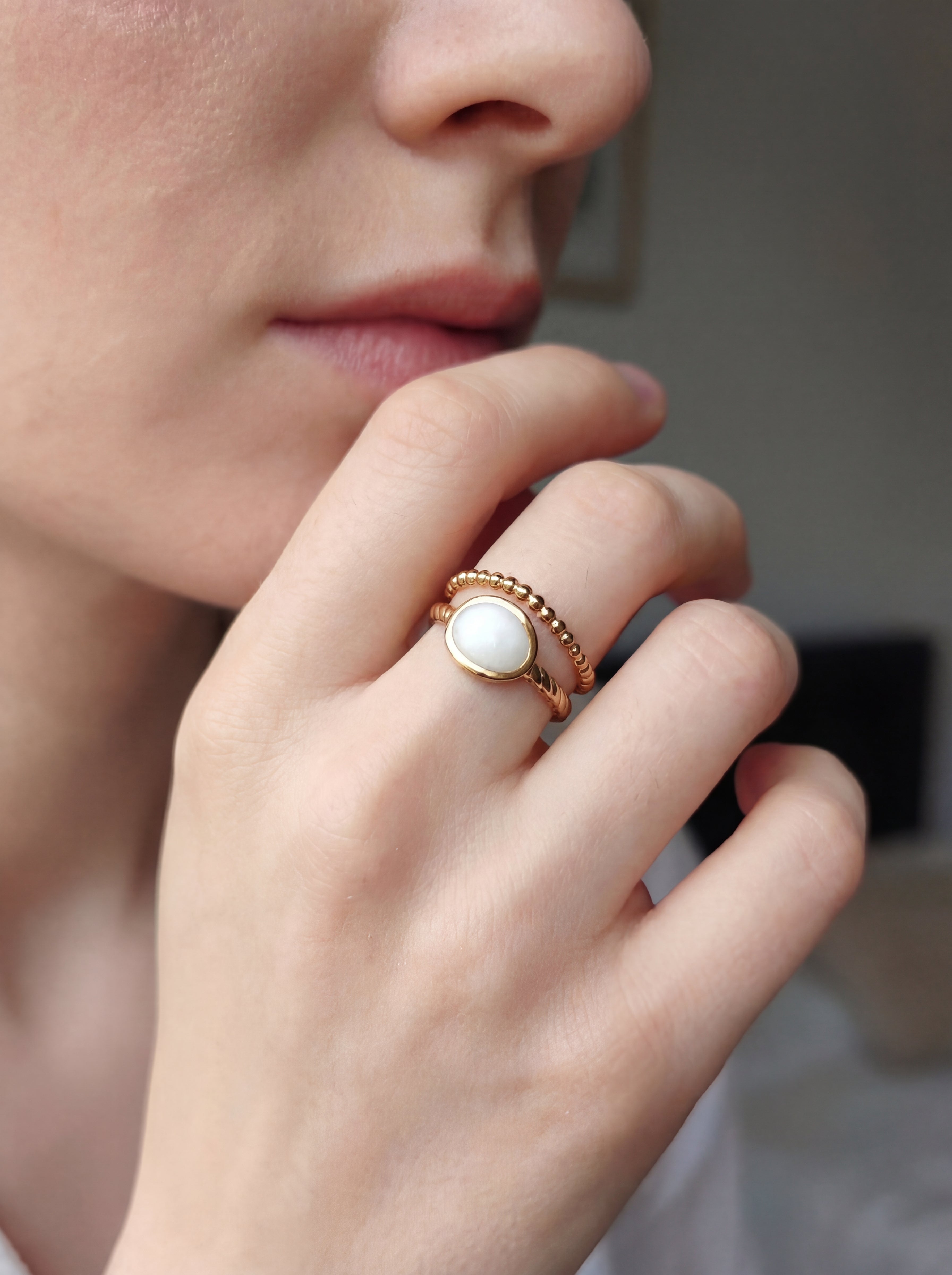 Close-up of a hand wearing a gold ring with a white stone, blurred background