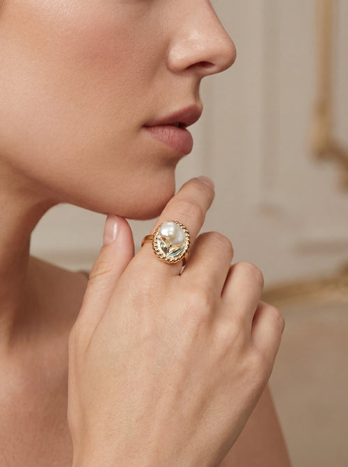 Close-up of a hand wearing a gold ring with a large gemstone, against a neutral background.