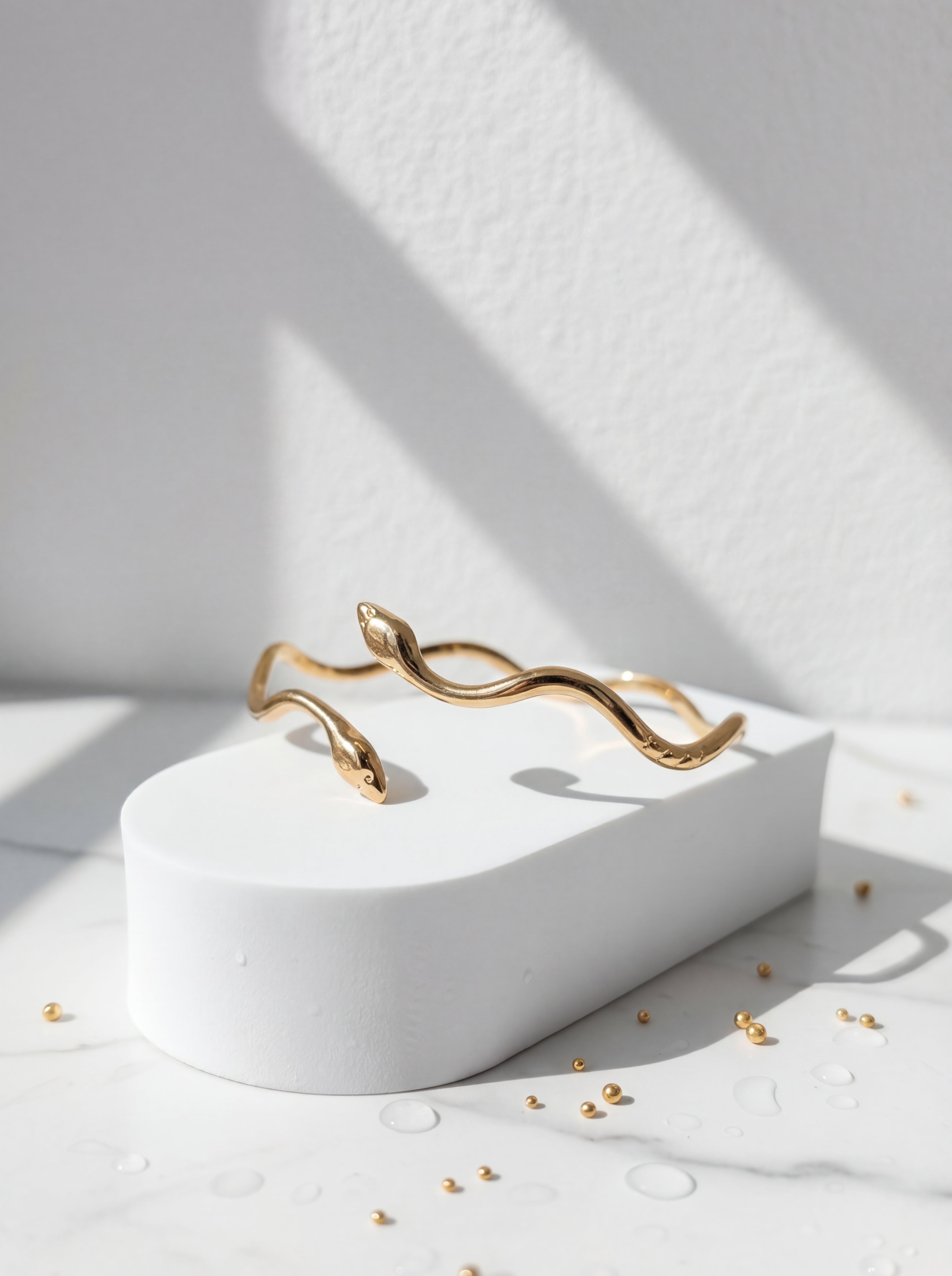 Gold bracelet on a white pedestal with a minimal background