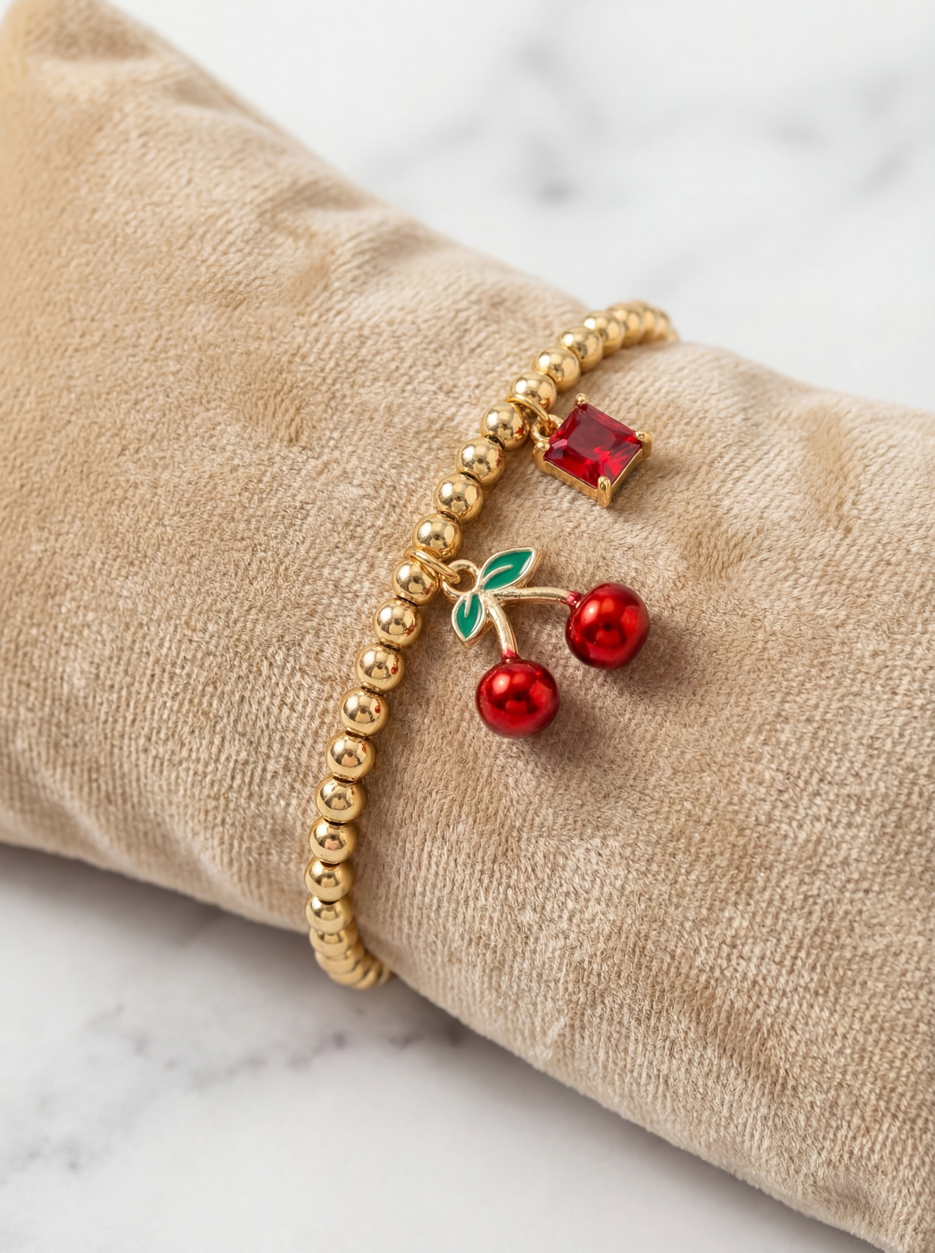 Gold bracelet with cherry charm on a beige cushion