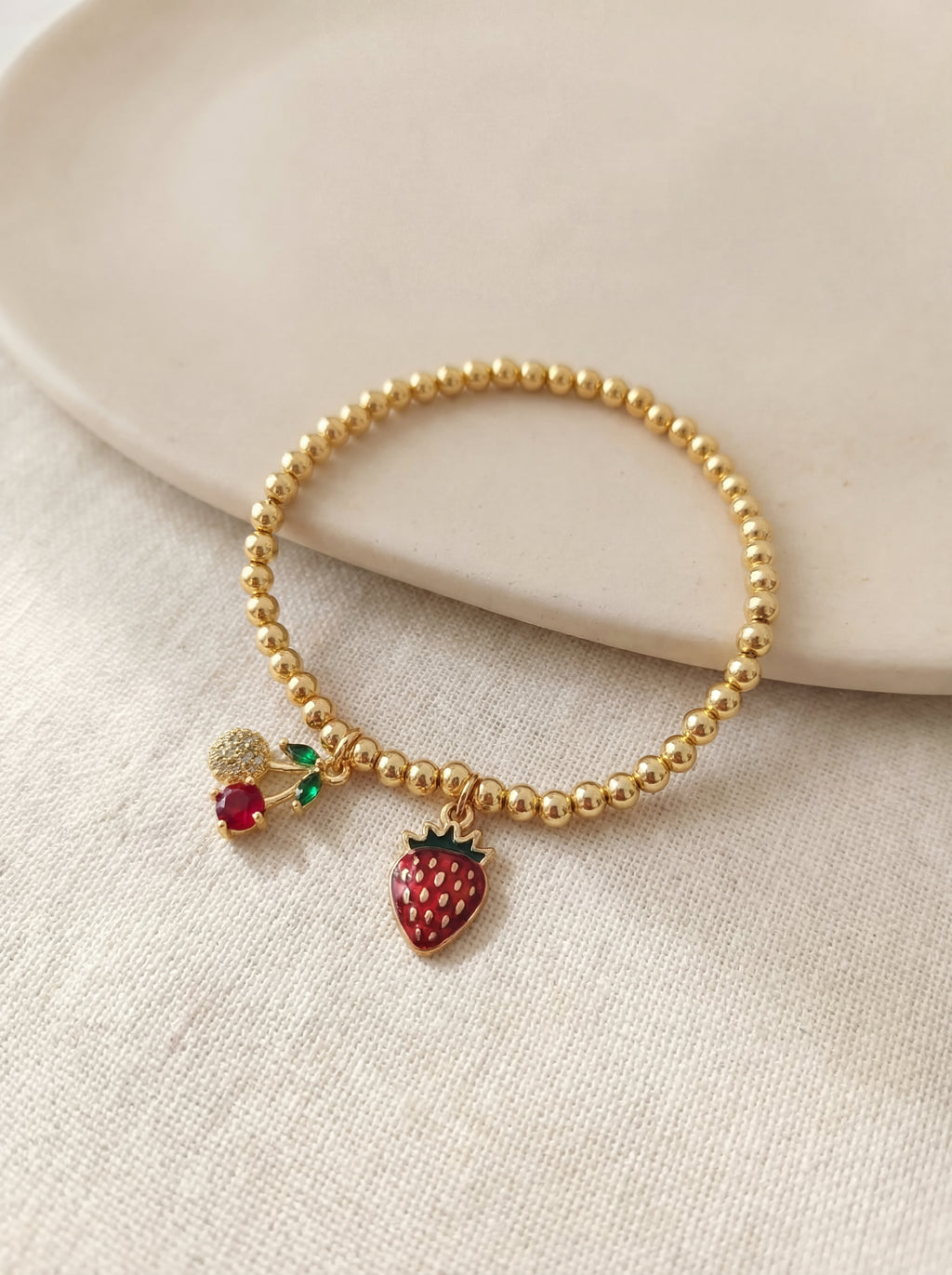 Gold beaded bracelet with strawberry charm on a beige surface