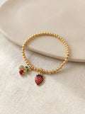 Gold beaded bracelet with strawberry charm on a beige surface