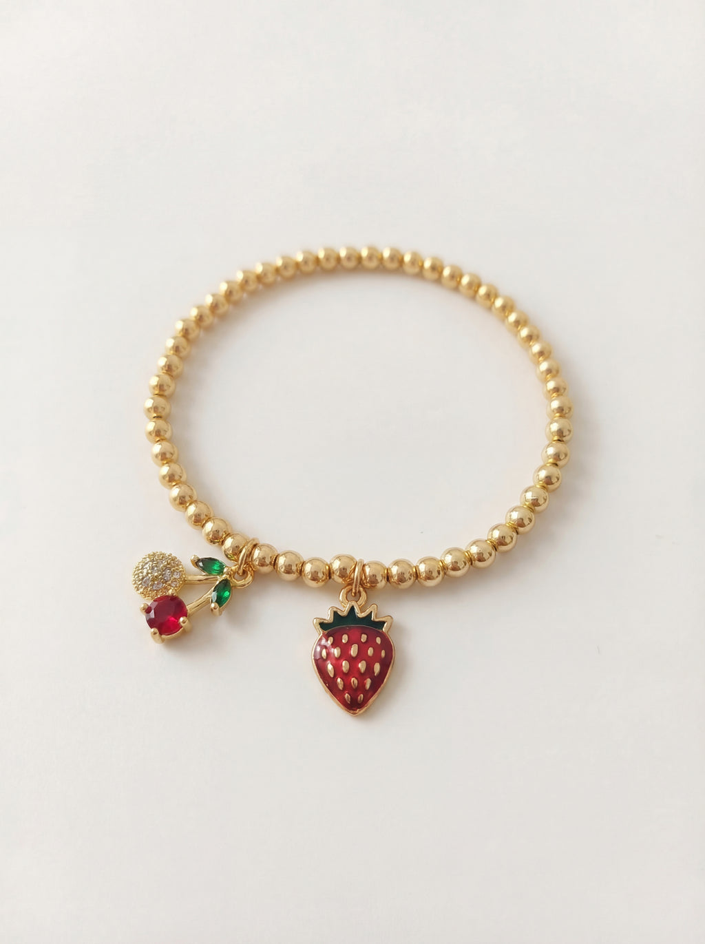 Gold beaded bracelet with strawberry charm on a light gray background