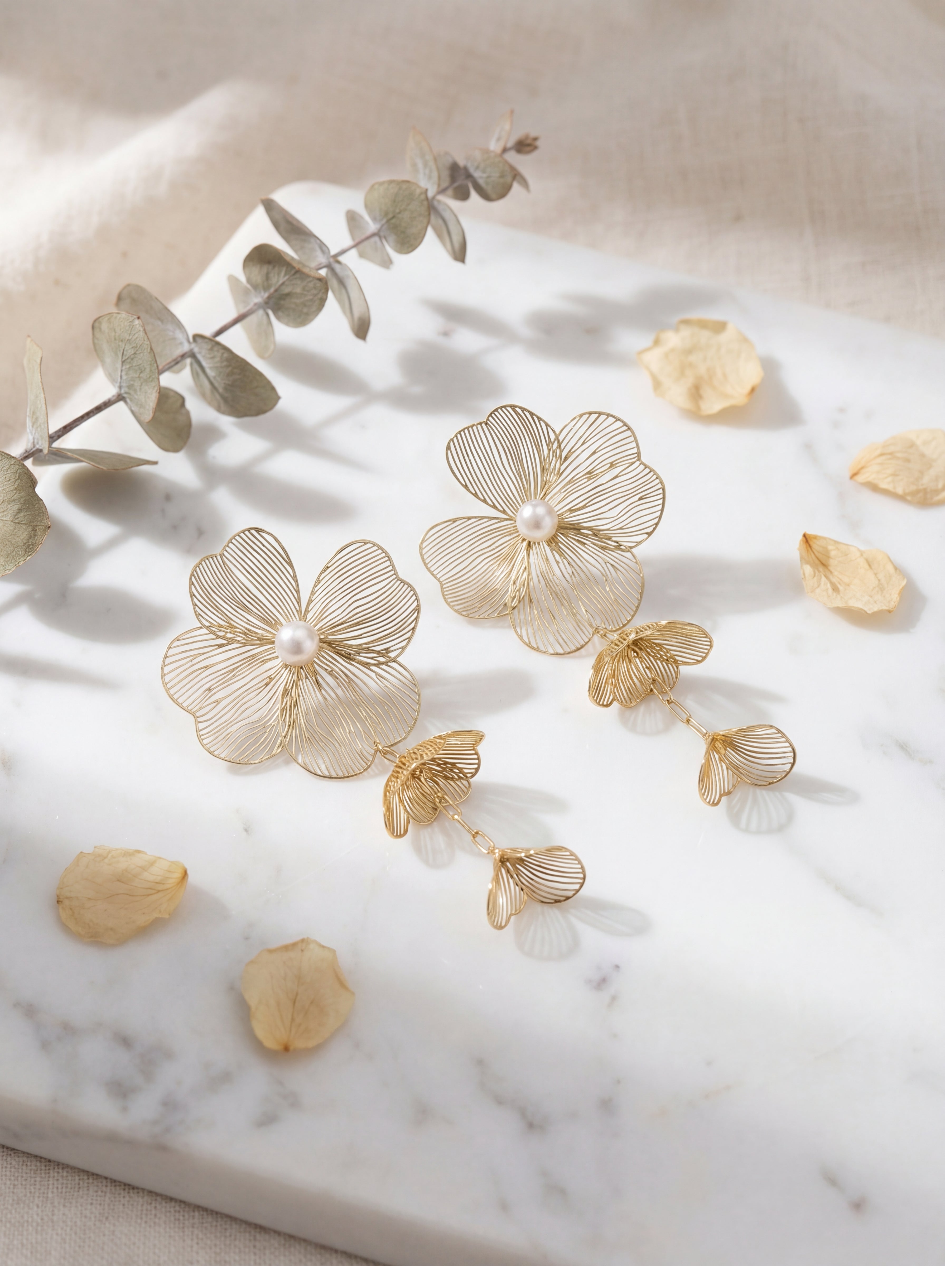 Gold floral earrings with pearls on a marble surface