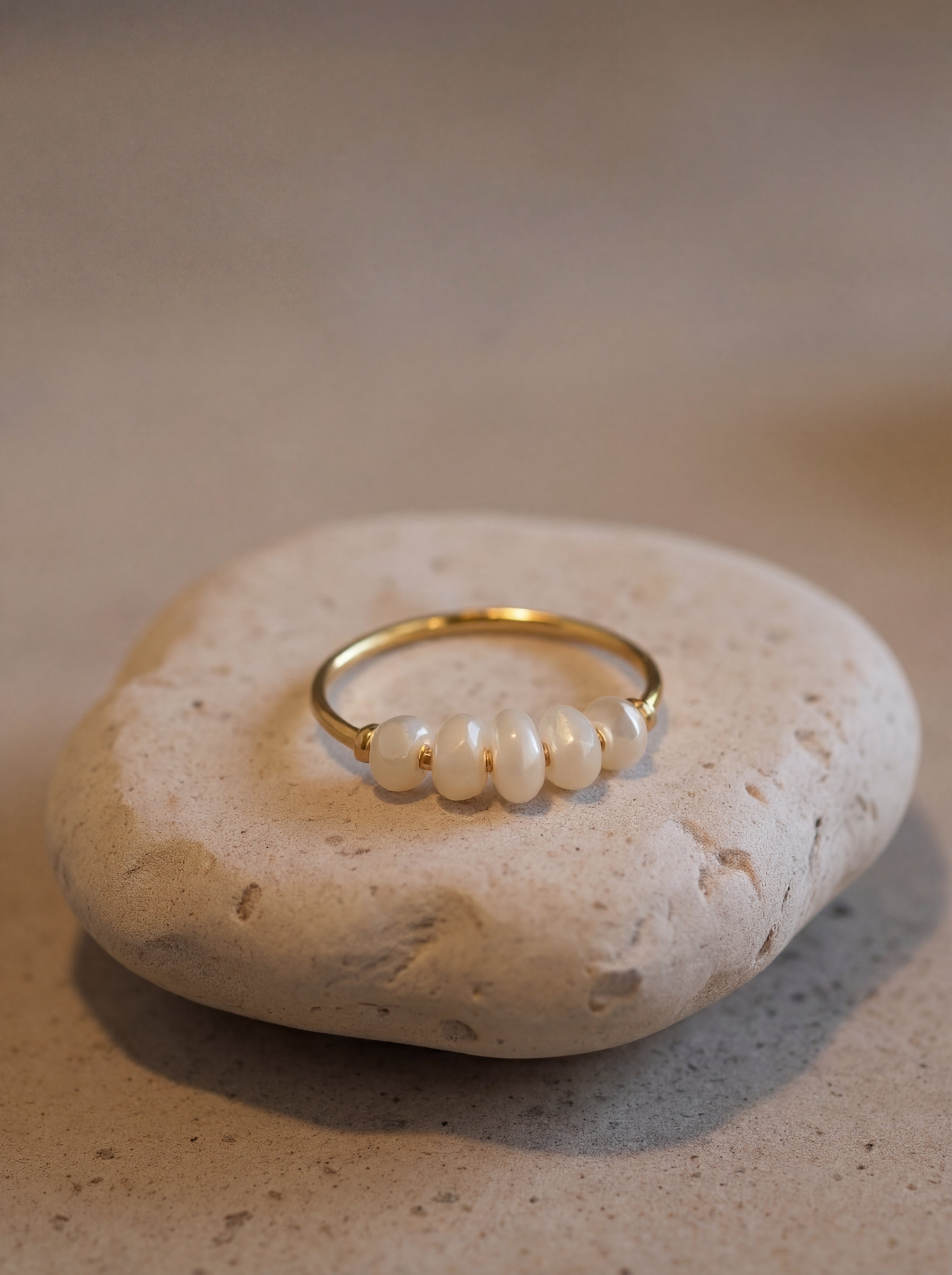 Gold ring with pearls on a beige stone surface