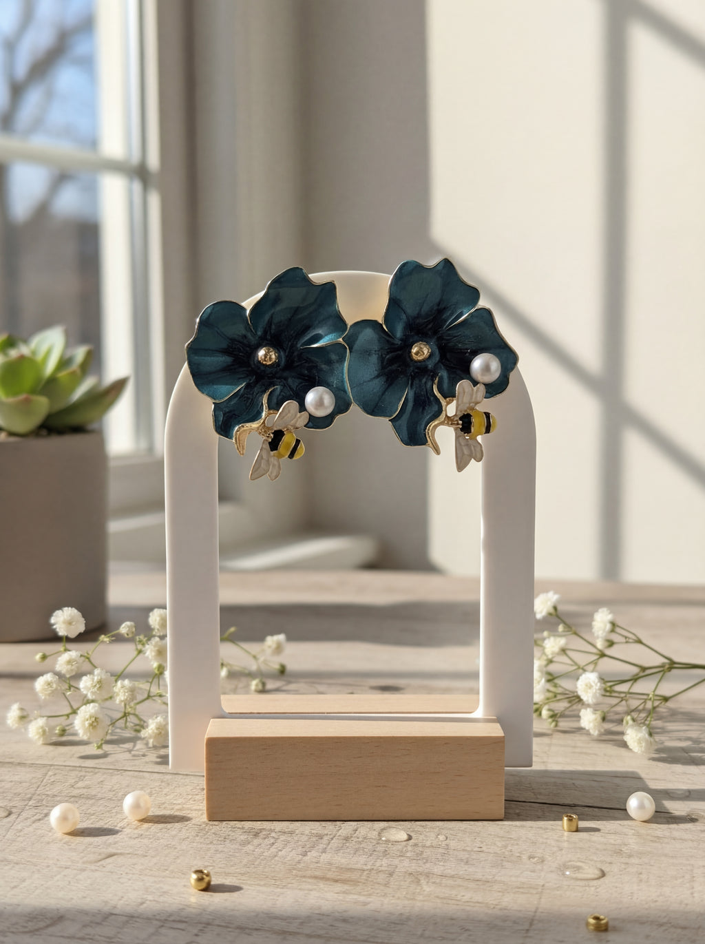 Pair of dark blue floral earrings on a white stand with a blurred indoor background