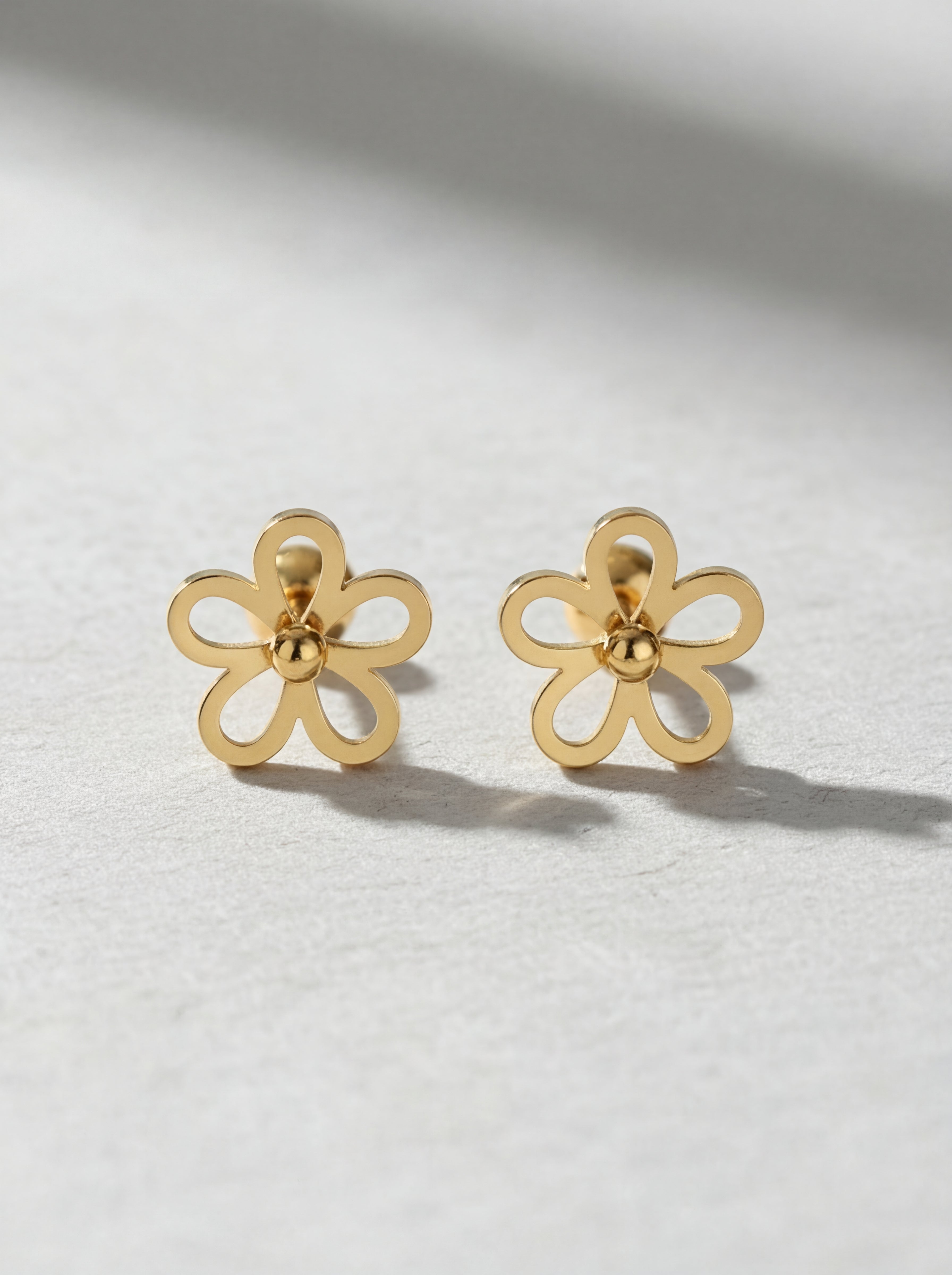 Gold flower-shaped earrings on a light gray background