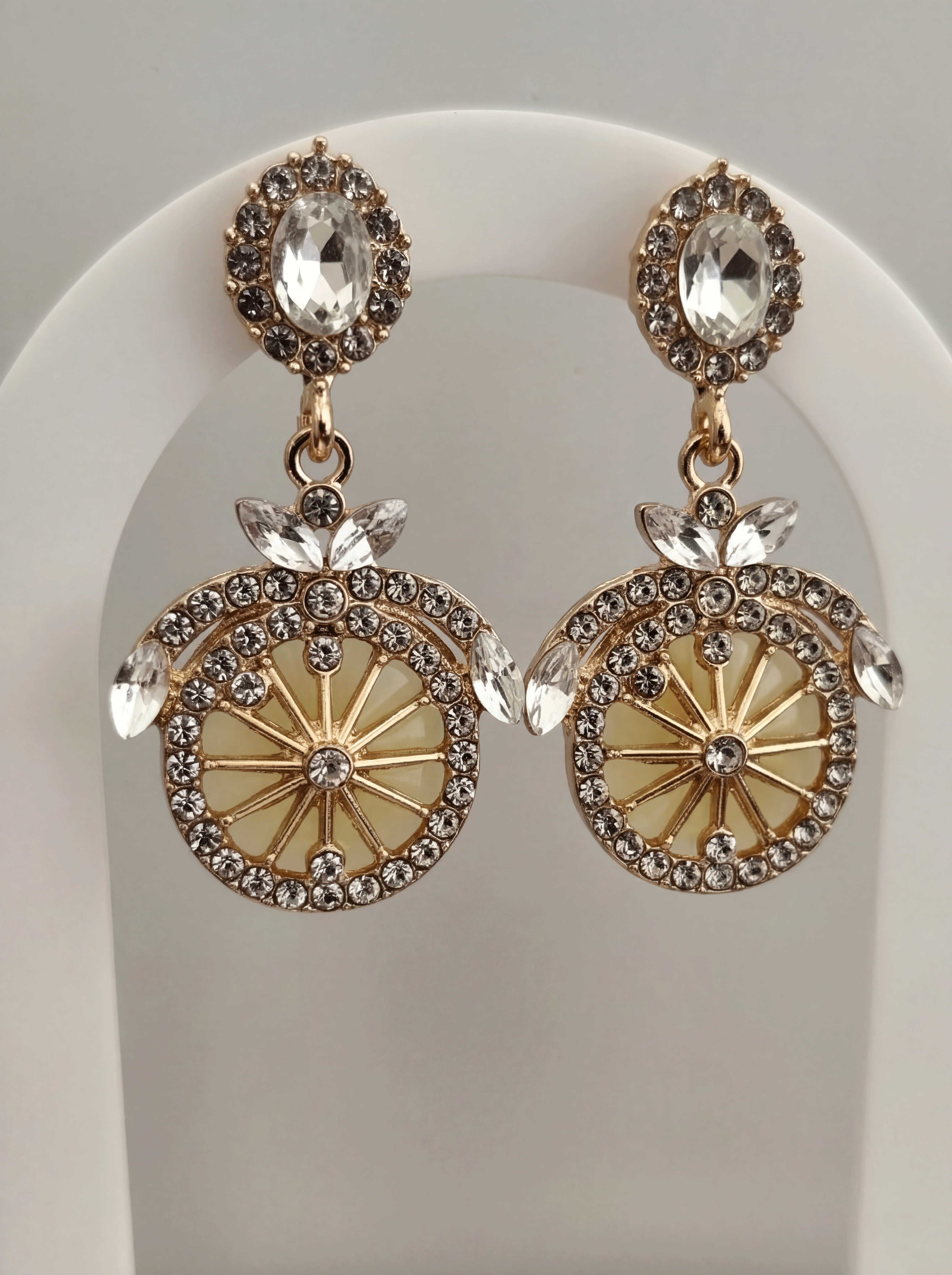 Ornate earrings with gold and crystal details on a white stand.