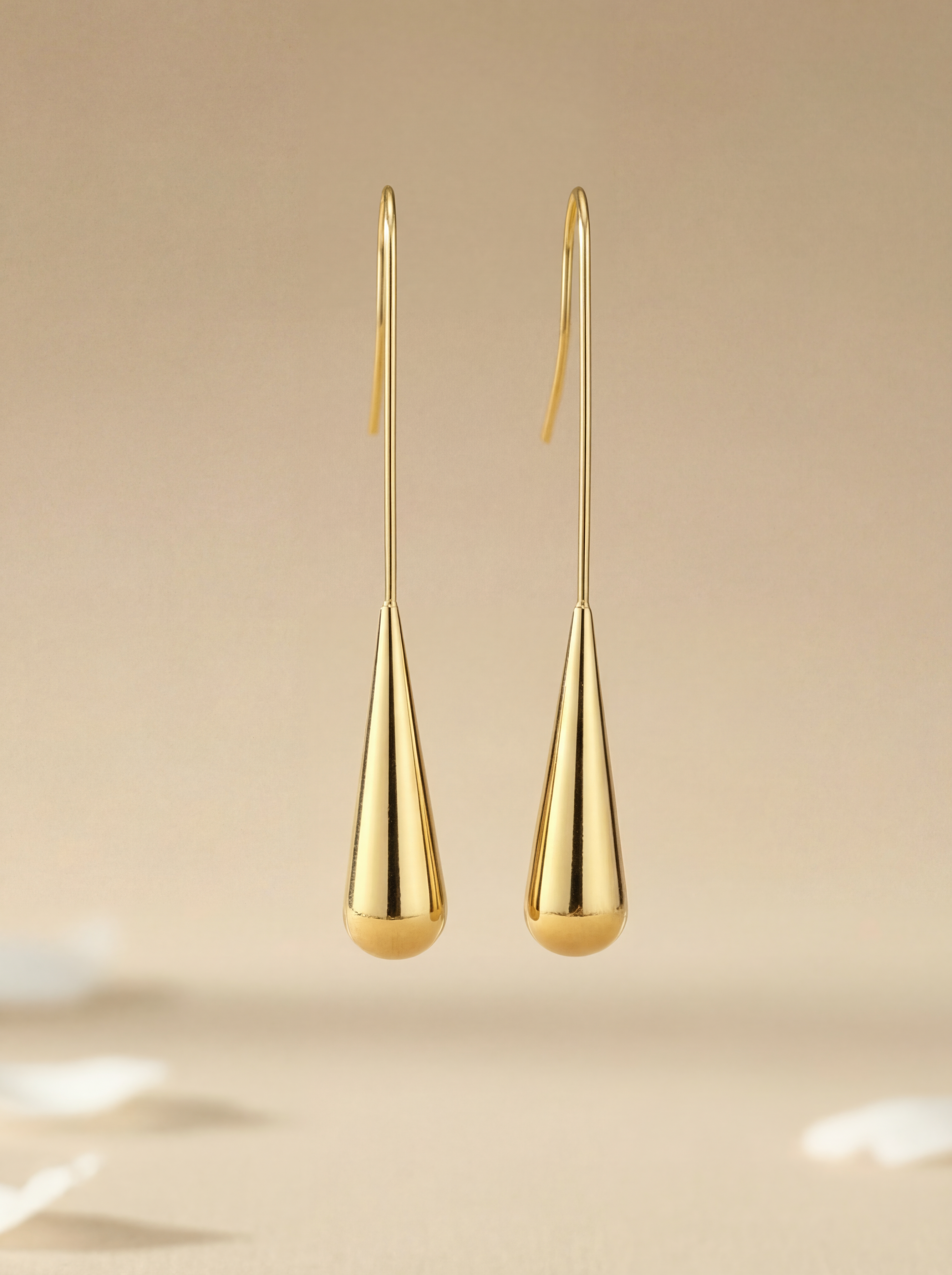Gold teardrop earrings on a beige background