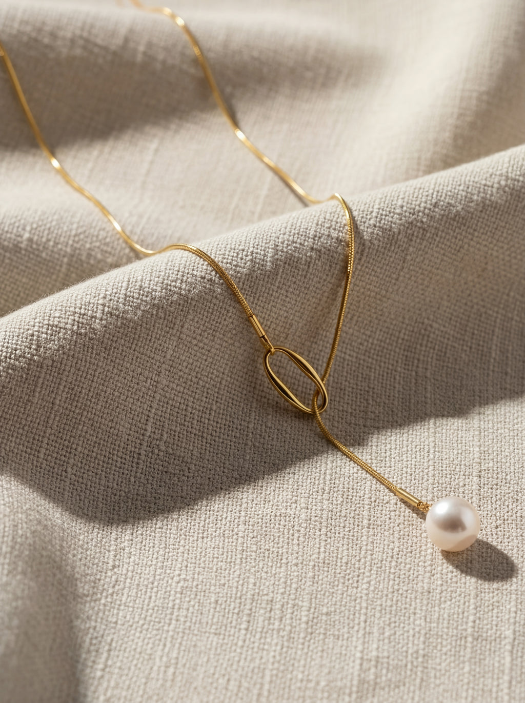 Gold necklace with a pearl pendant on a beige fabric background
