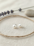 Pearl stud earrings on a beige surface with lavender and stones in the background