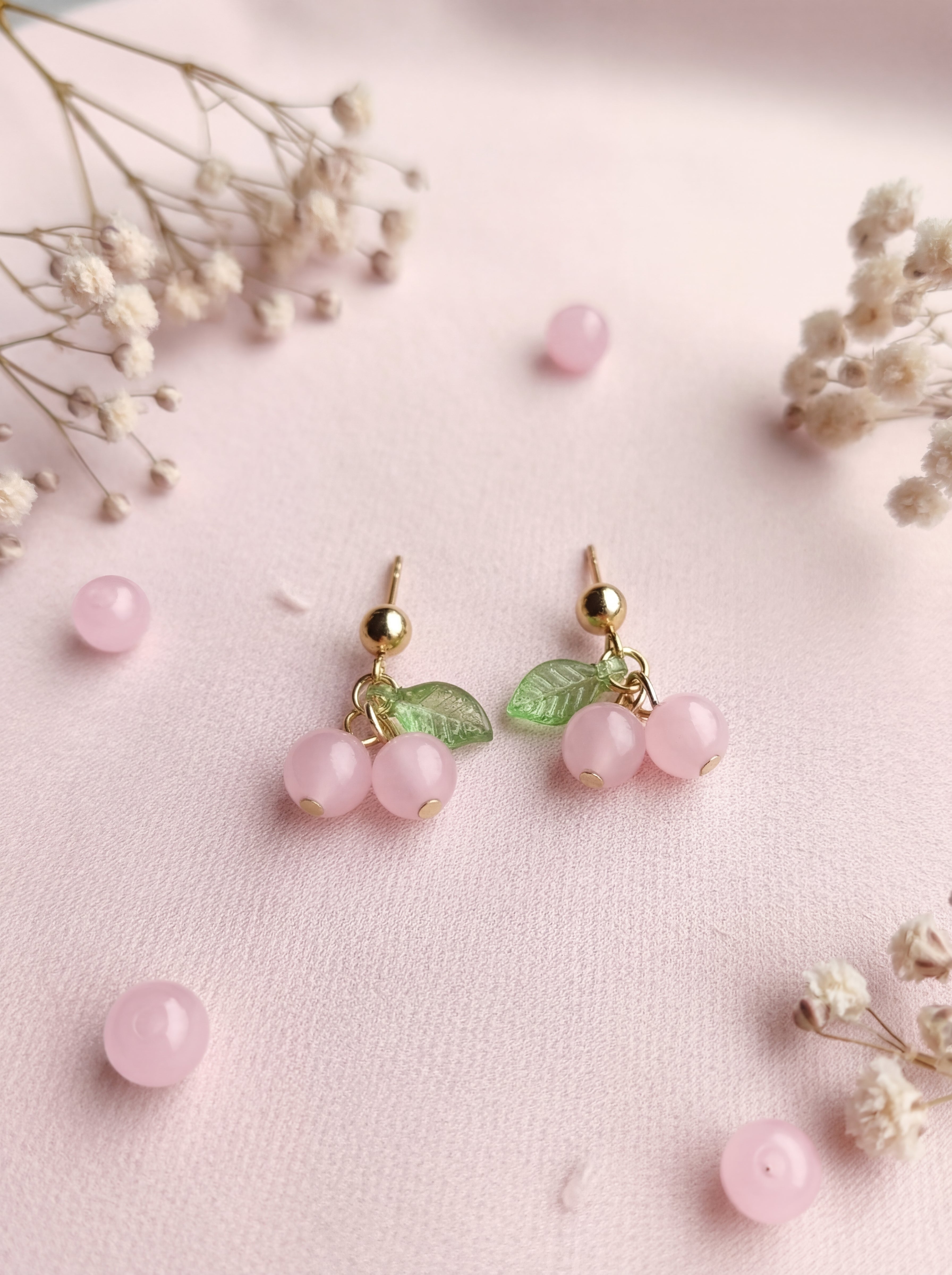 Pink berry earrings with gold accents on a pink background with small flowers.