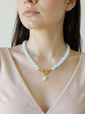 Woman wearing a delicate necklace with a pearl pendant against a neutral background