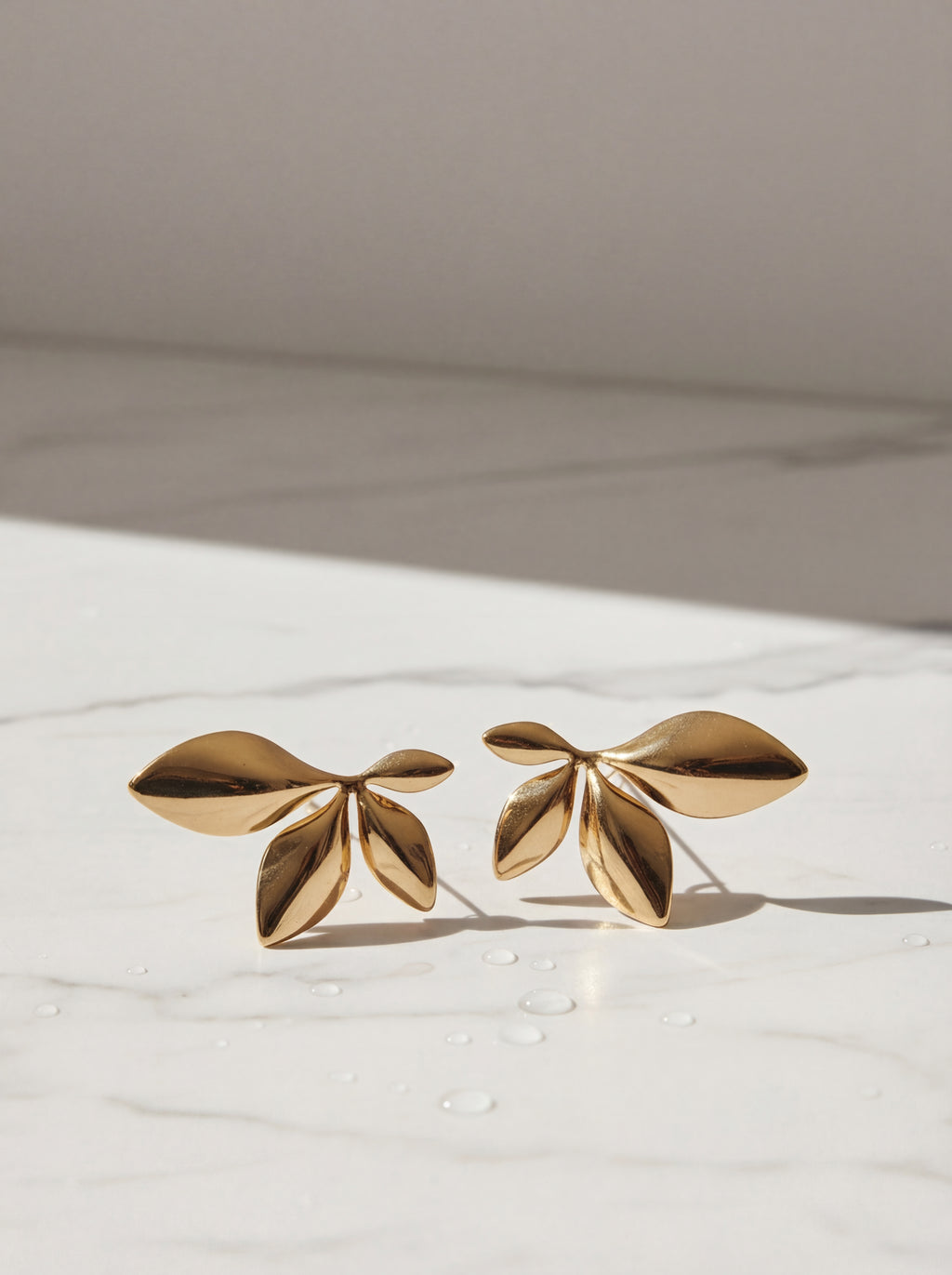 Gold leaf-shaped earrings on a light background