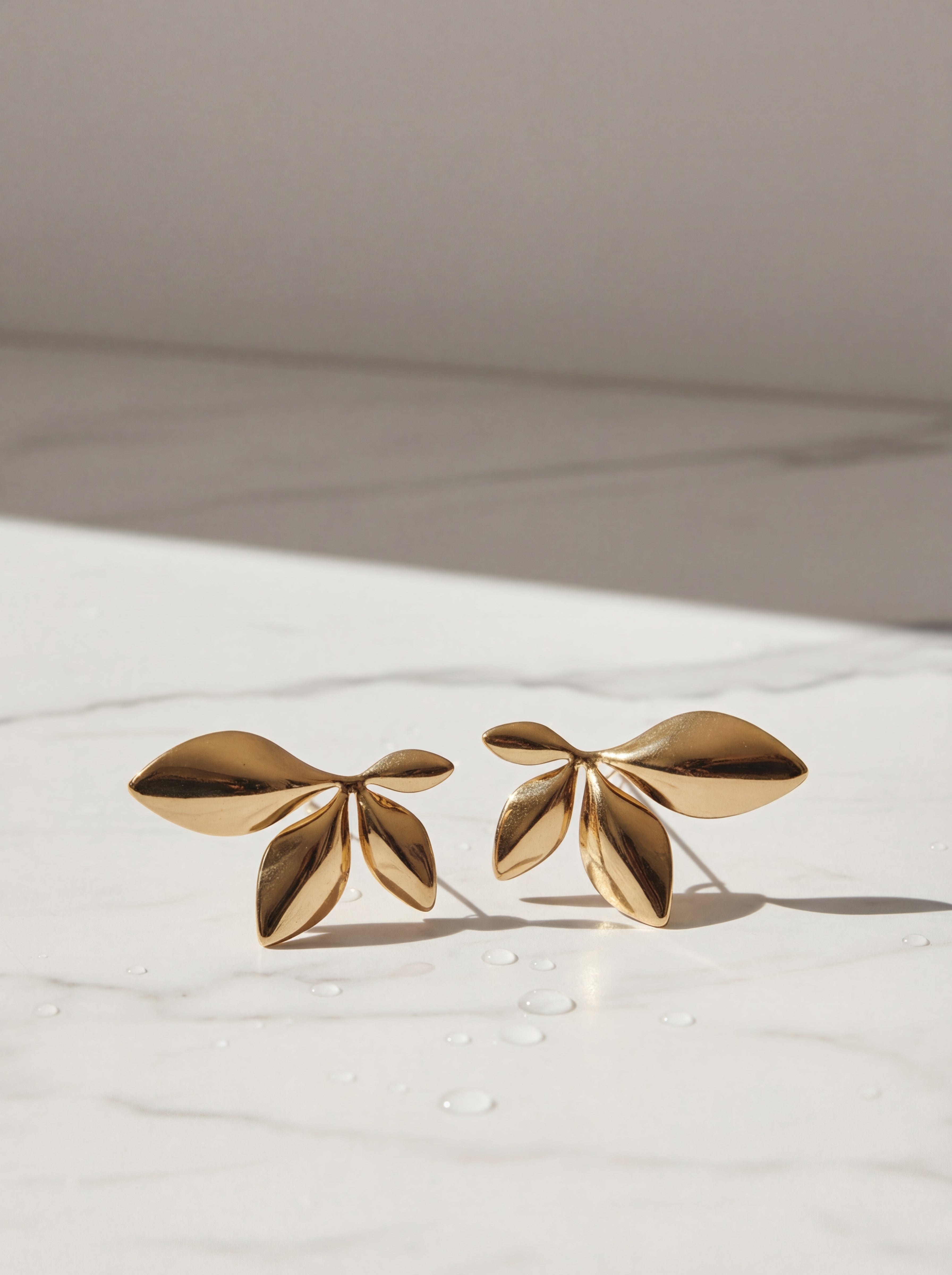 Gold leaf-shaped earrings on a light background