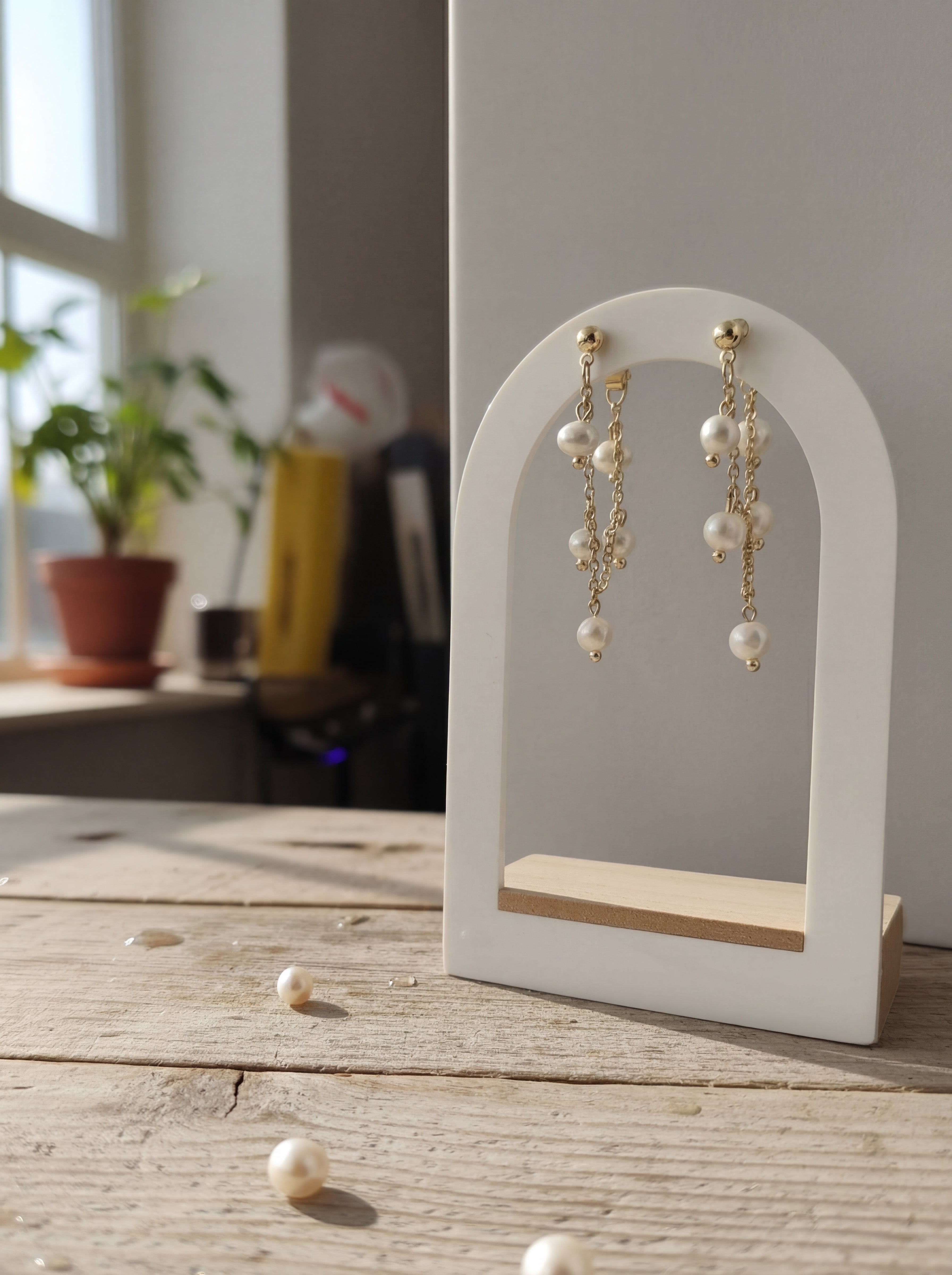 Pearl earrings on a white stand with scattered pearls on a wooden surface.