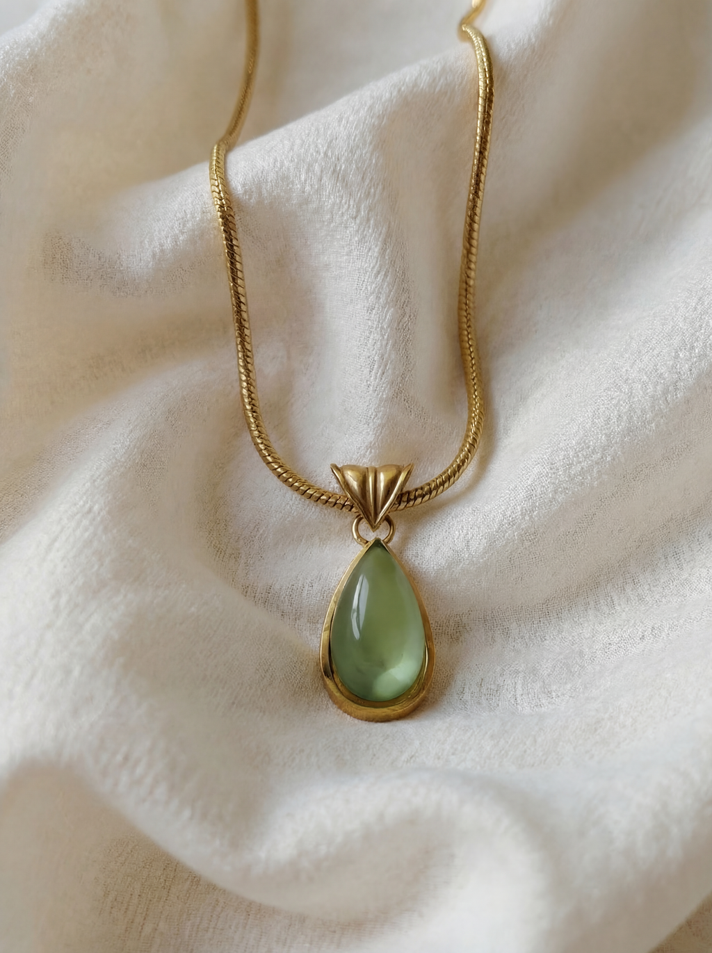 Gold necklace with a green teardrop pendant on a white fabric background