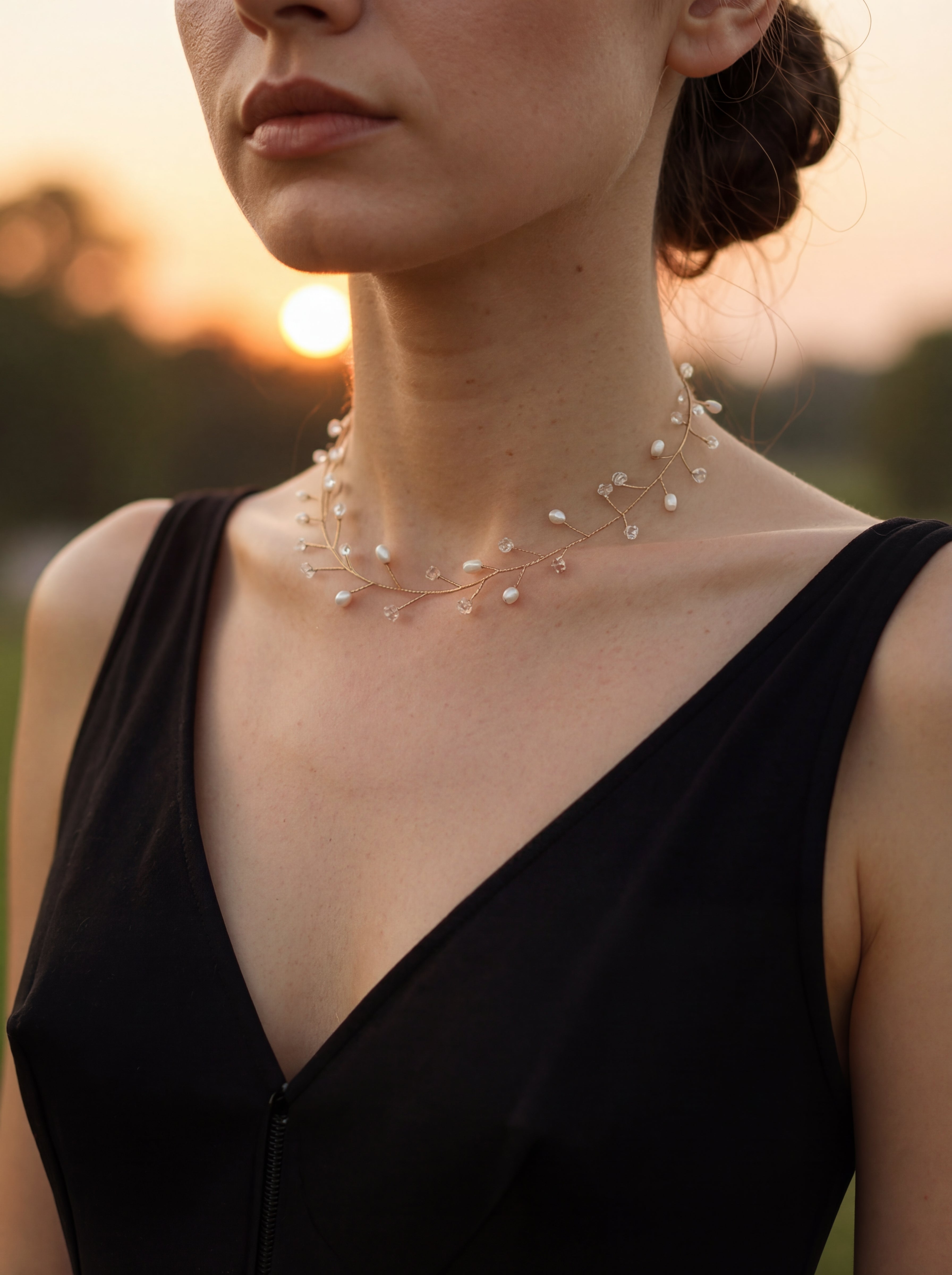 Woman wearing a delicate necklace with a blurred sunset background
