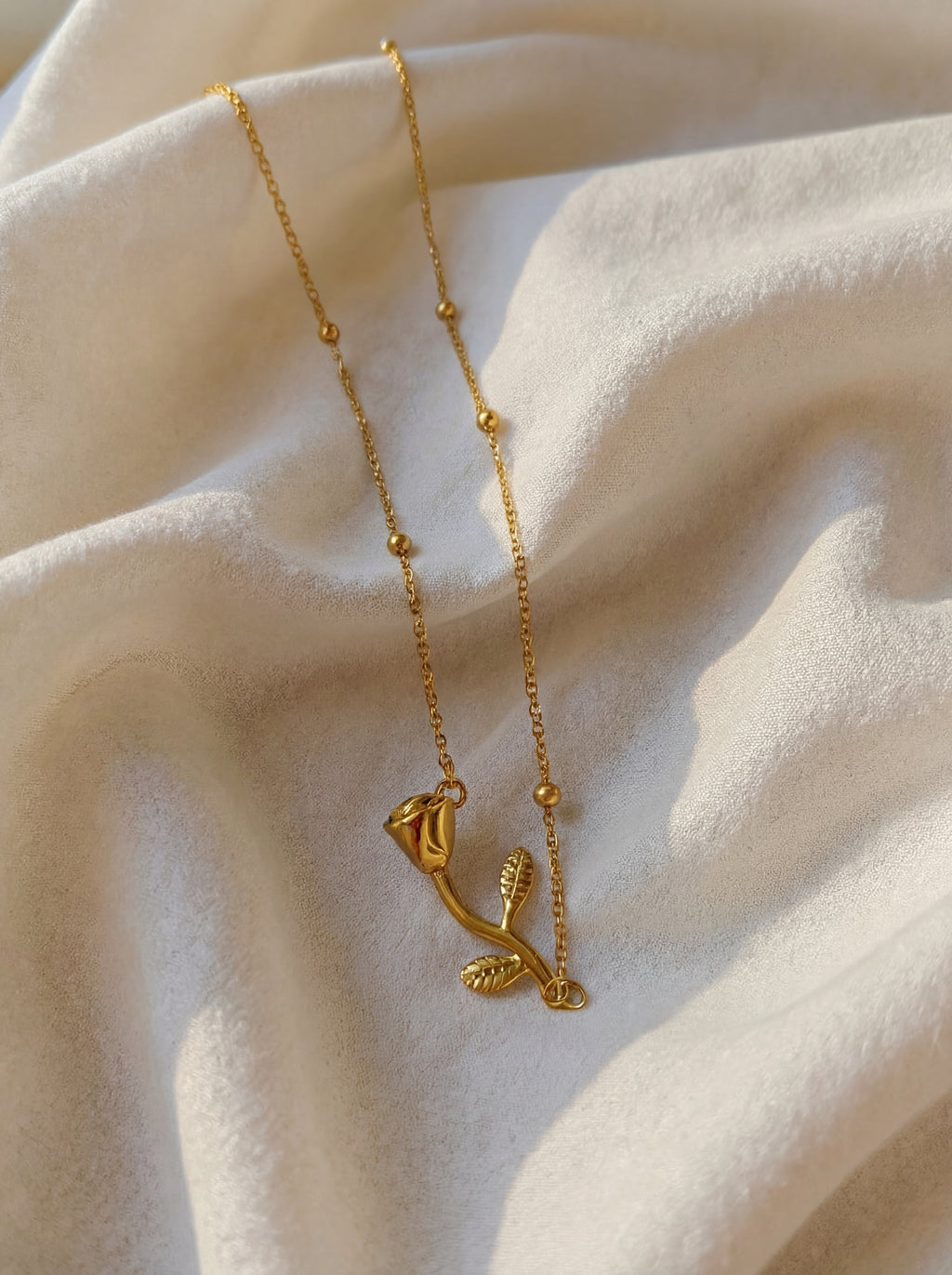 Gold necklace with a delicate pendant on a soft beige fabric background