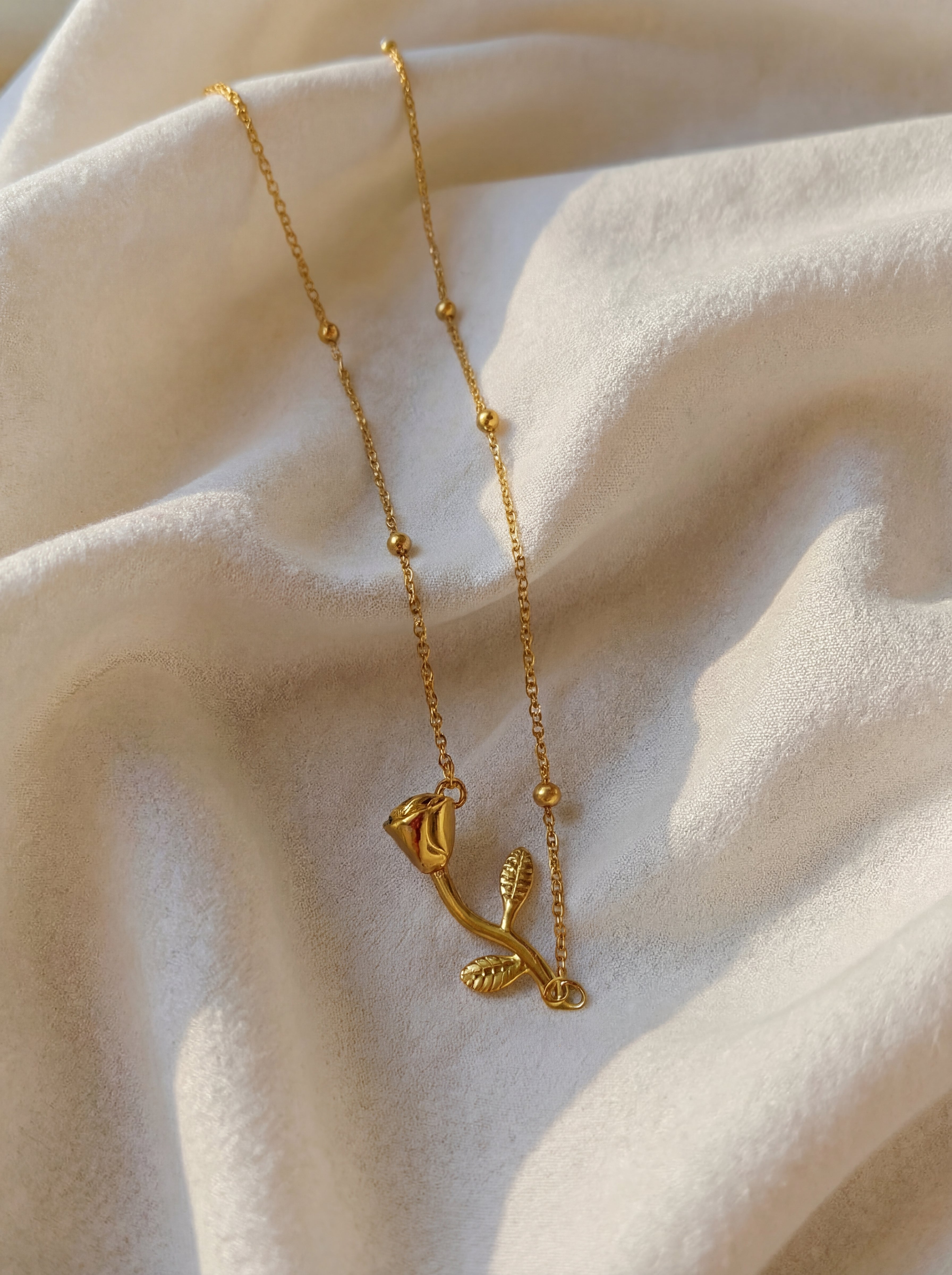 Gold necklace with a delicate pendant on a soft beige fabric background