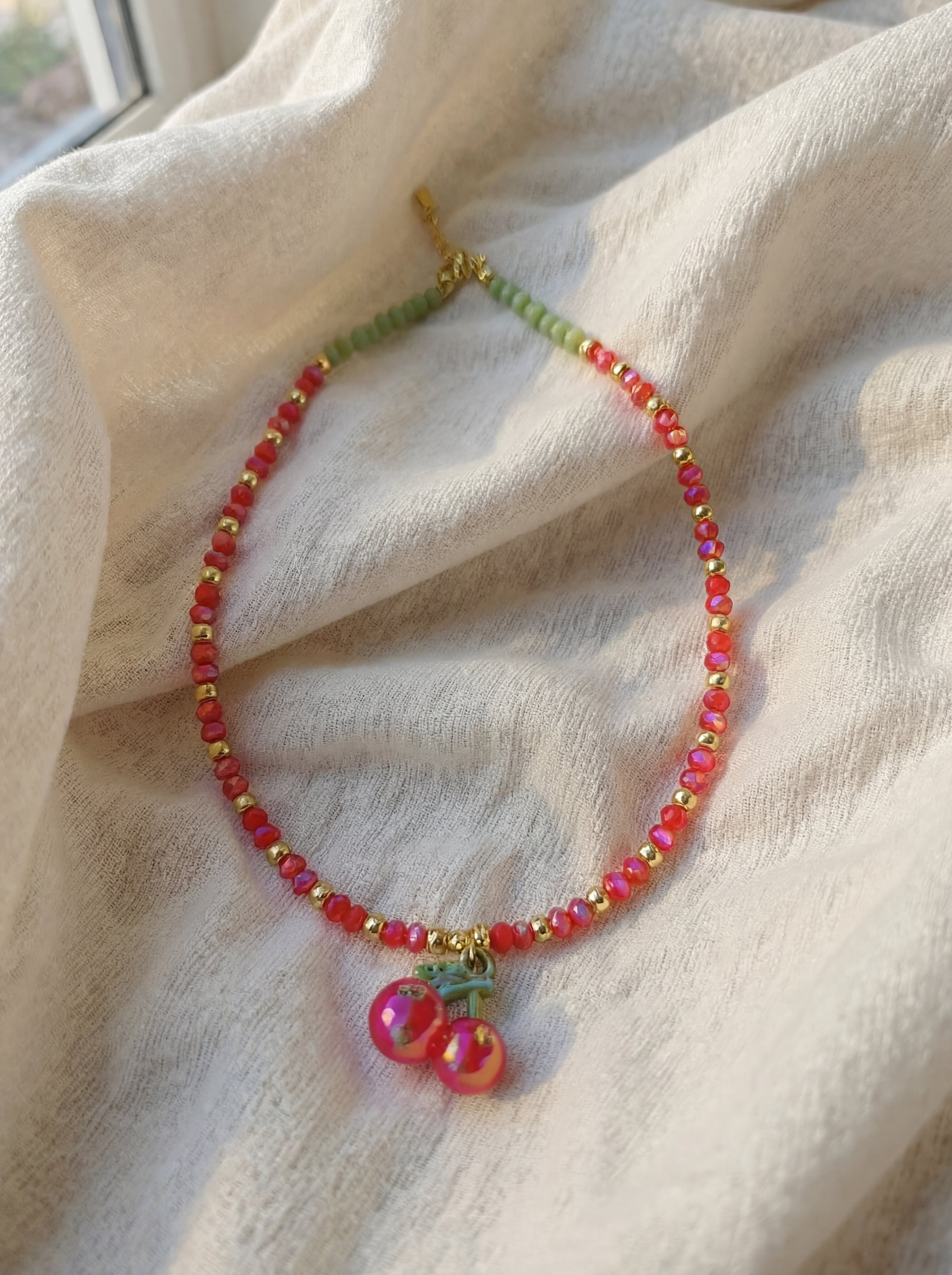 Beaded necklace with cherry charm on a textured fabric background