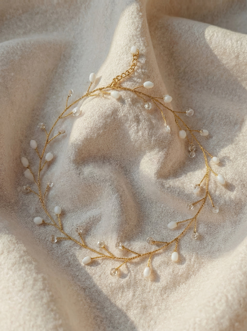 Delicate gold necklace with small pearls on a soft beige fabric background
