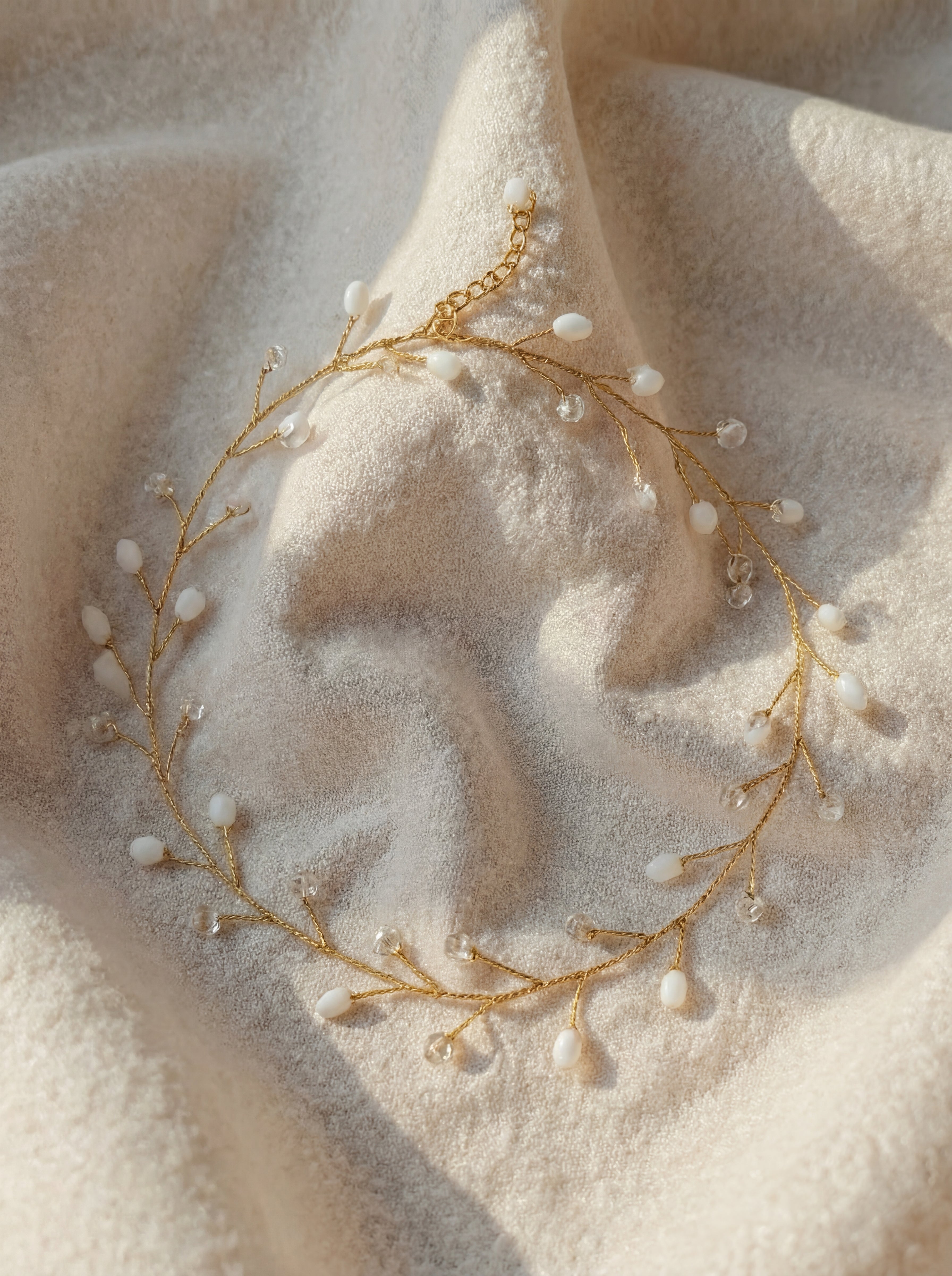 Delicate gold necklace with small pearls on a soft beige fabric background