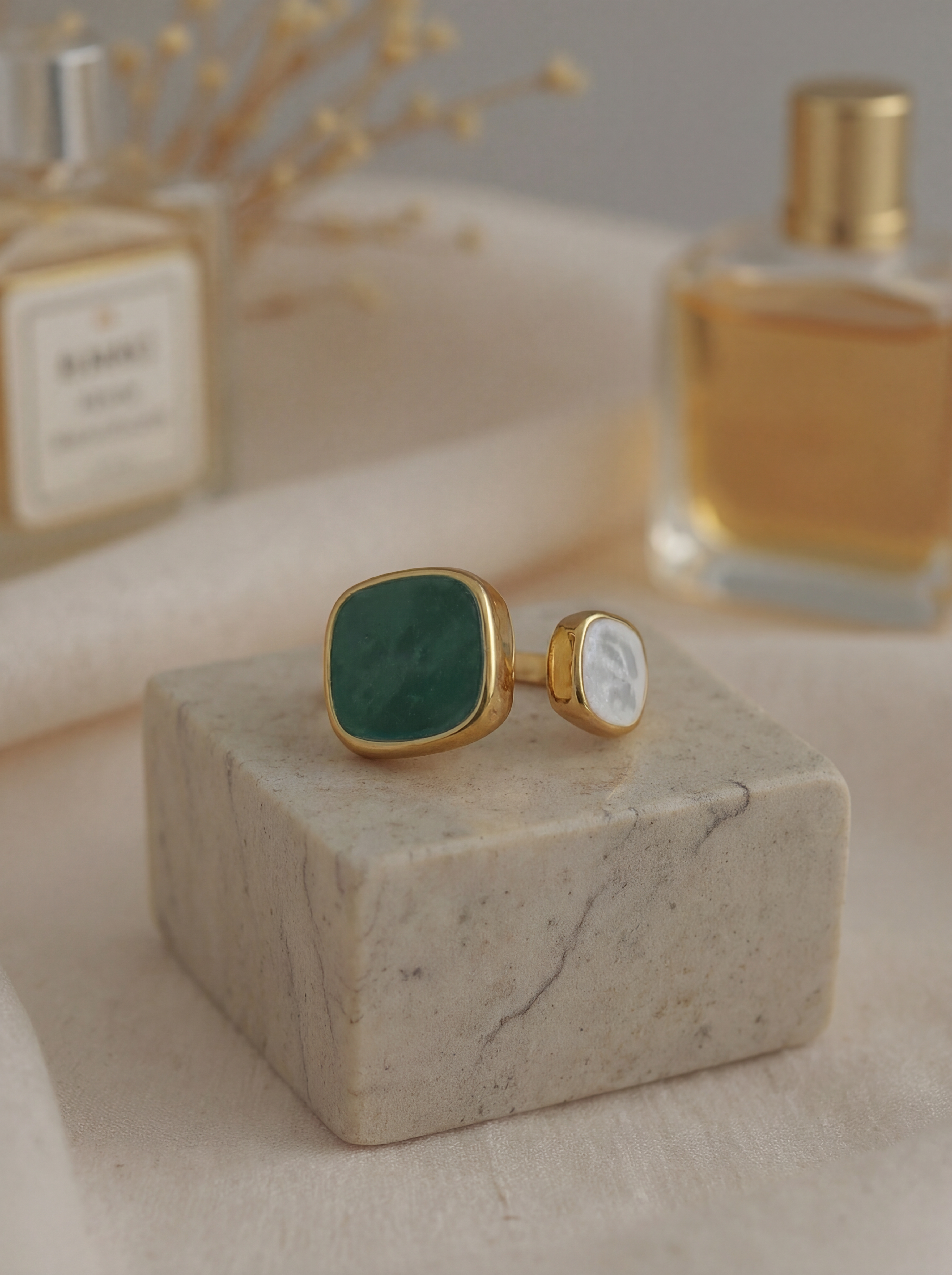 Gold cufflinks with green stone on a marble block with perfume bottles in the background