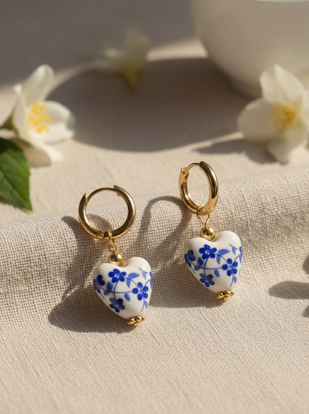 Heart-shaped earrings with blue floral design on a beige fabric background with flowers.