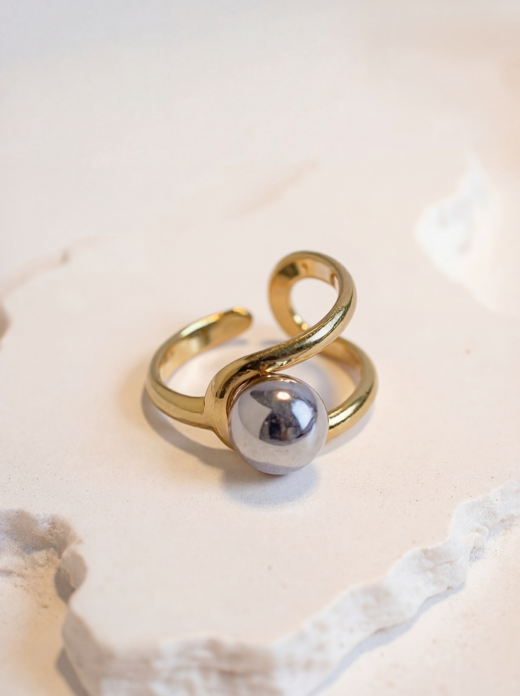Gold ring with a silver sphere on a light background