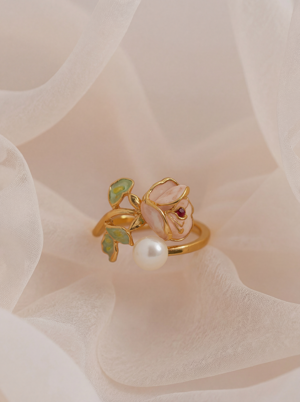 Gold ring with a pearl and green gemstone on a soft pink fabric background