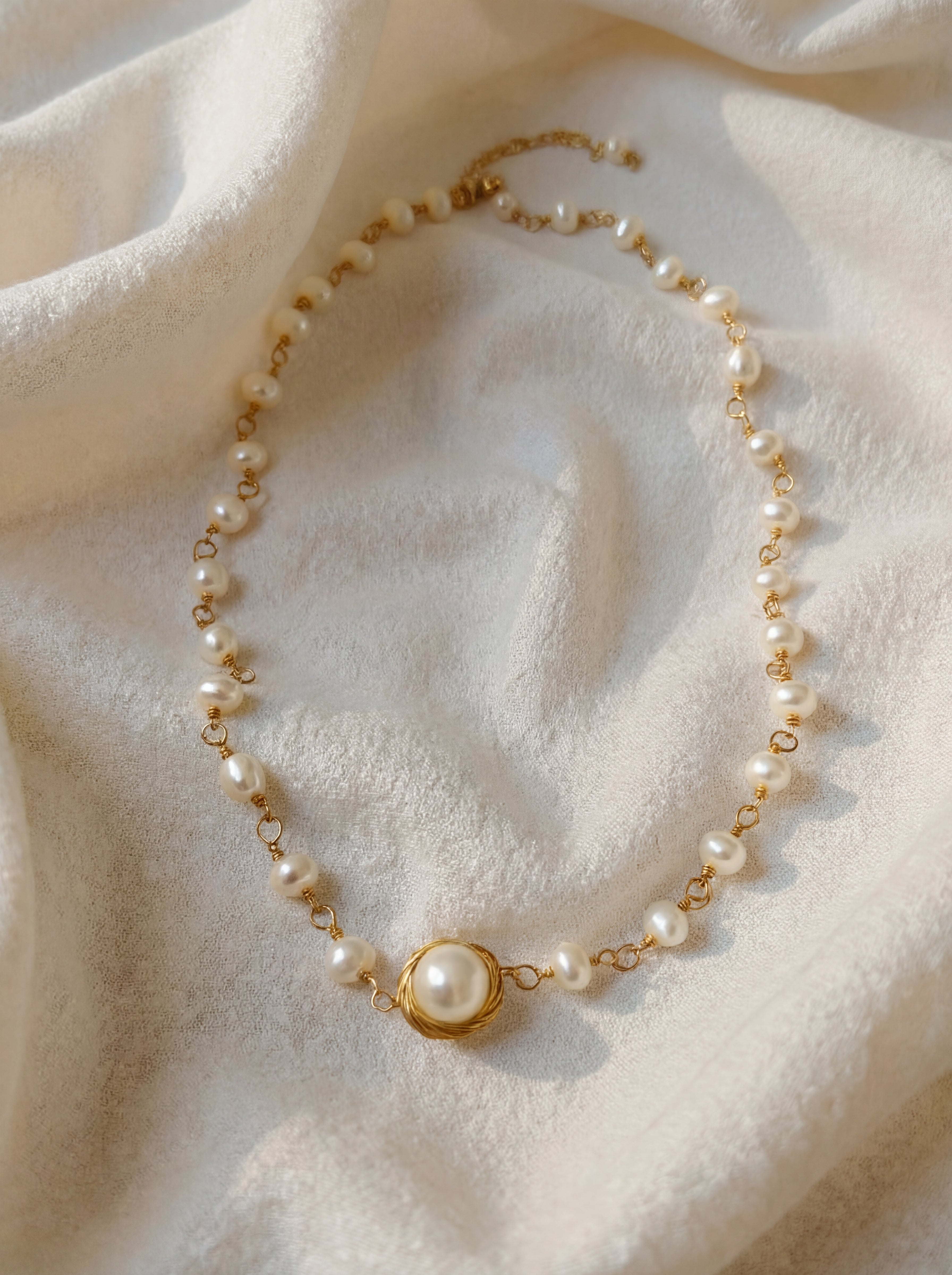 Pearl necklace with gold chain on a soft beige fabric background