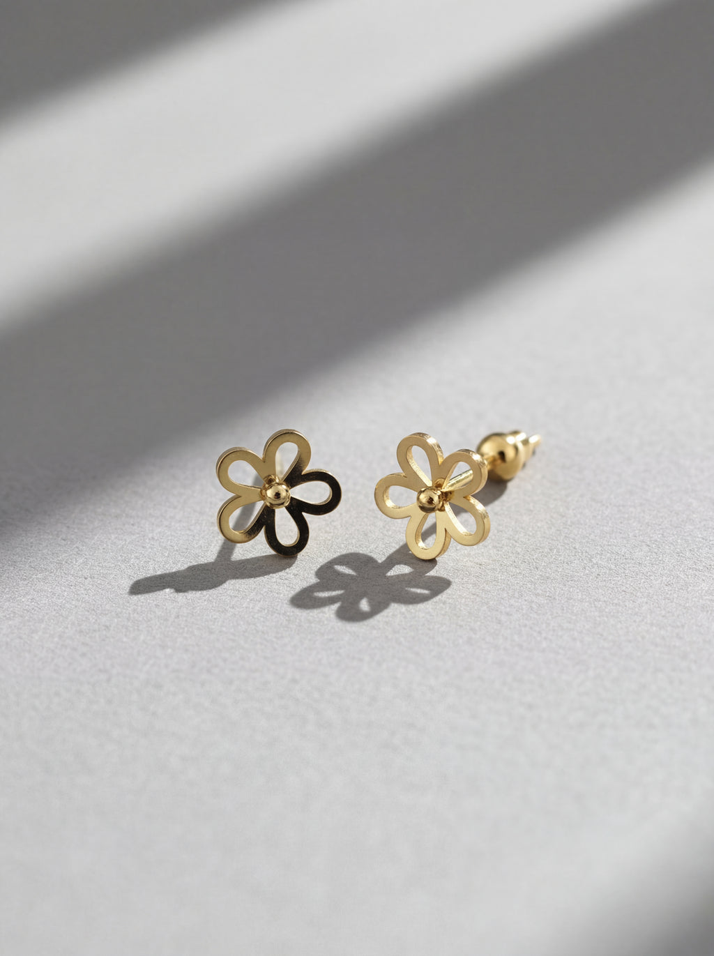 Gold flower-shaped earrings on a light gray surface with soft shadows.
