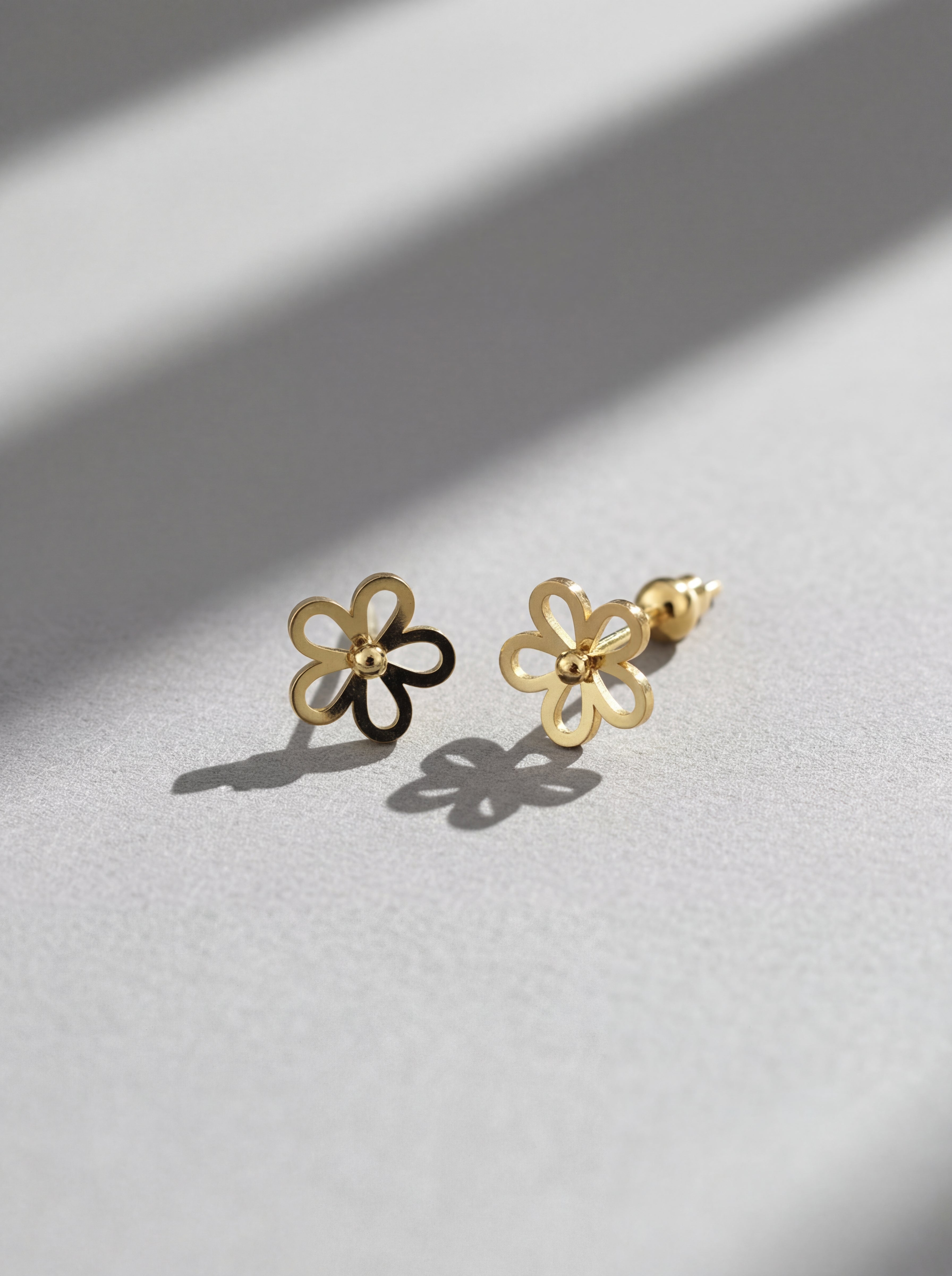 Gold flower-shaped earrings on a light gray surface with soft shadows.