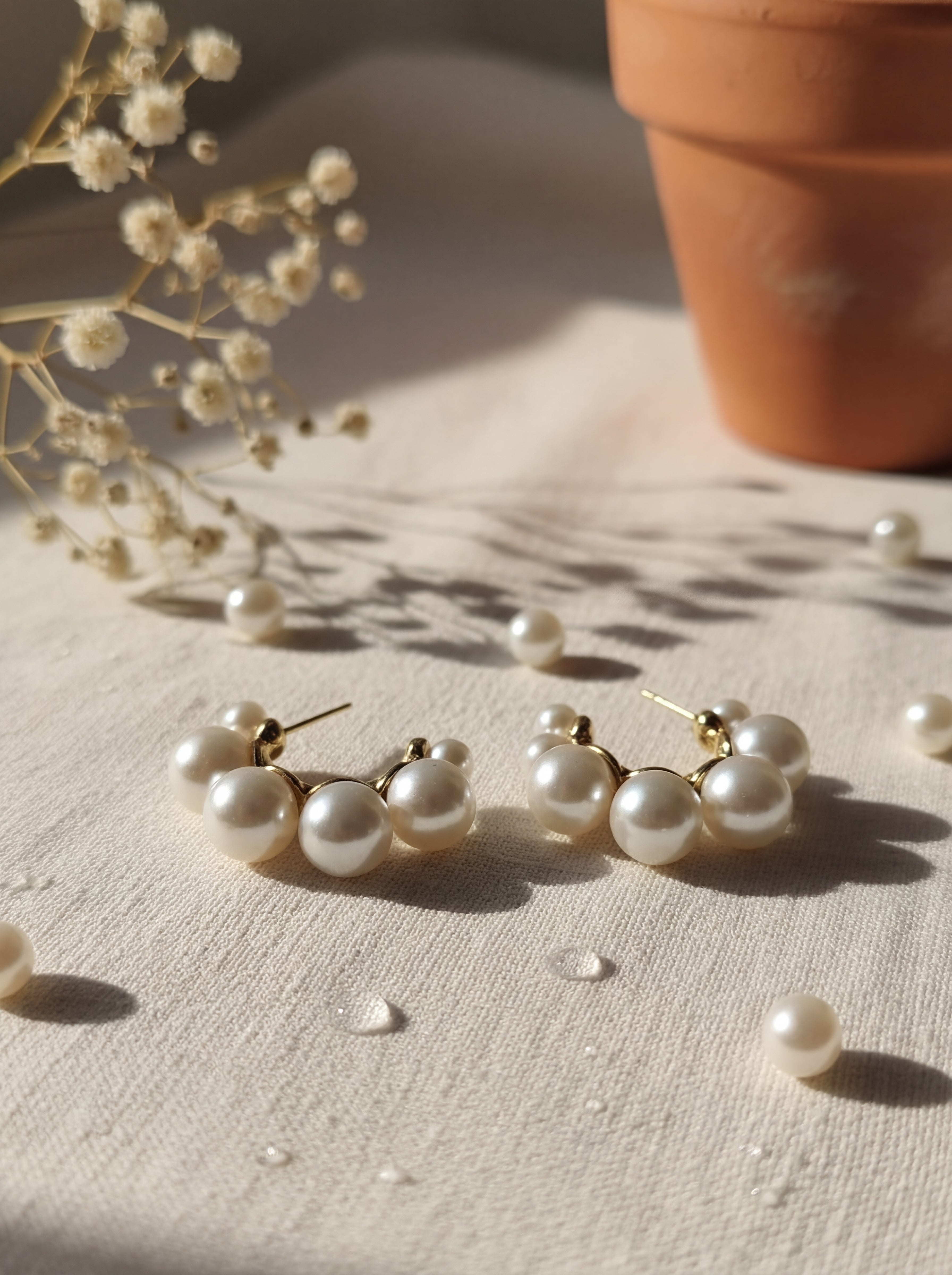 Pearl earrings on a textured surface with a potted plant in the background