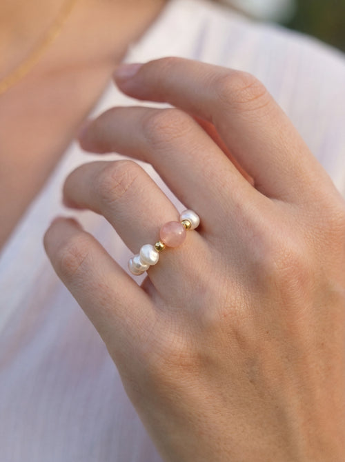 Close-up of a hand wearing a ring with pearls and pink stone.