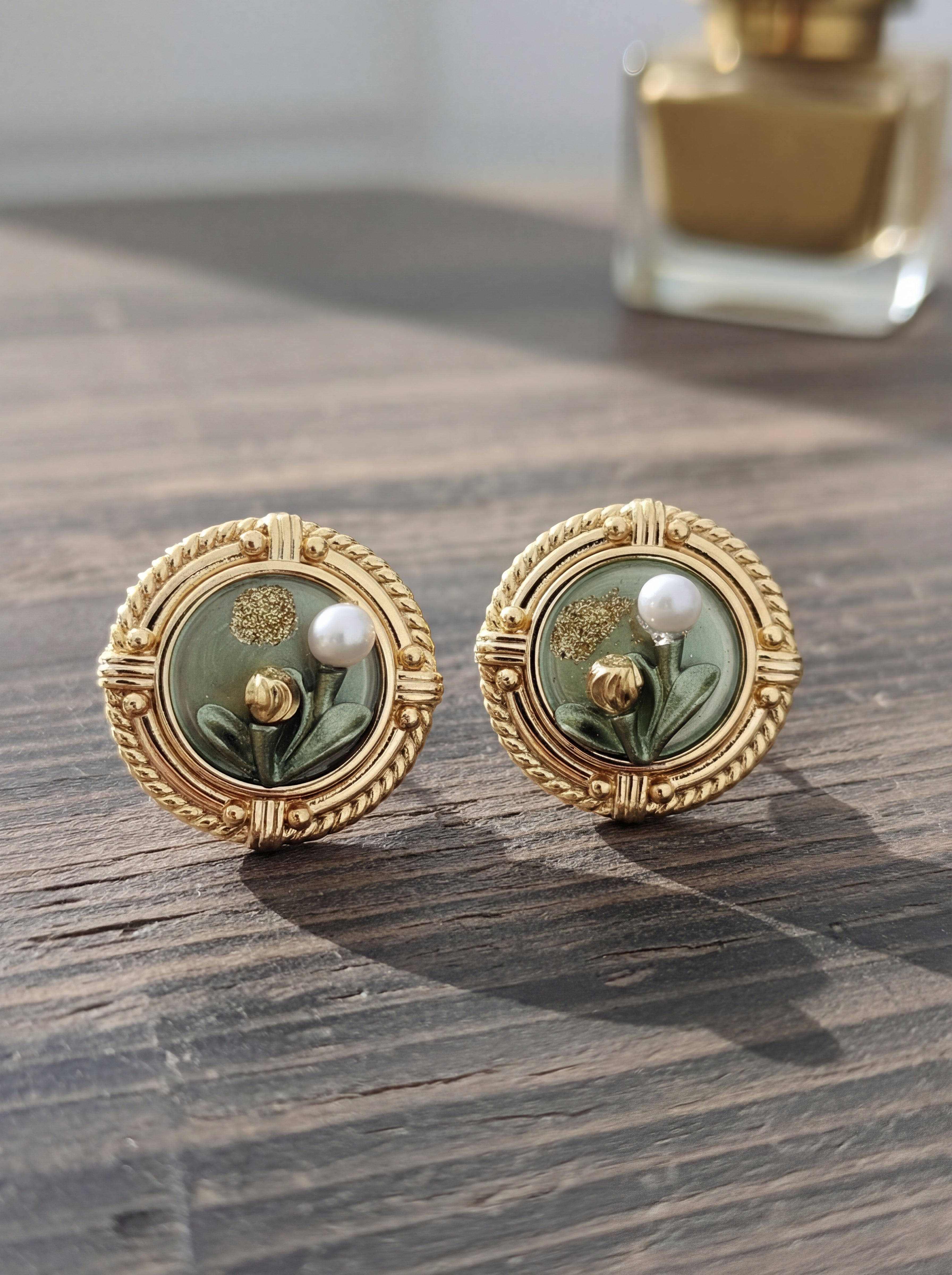 Pair of gold earrings with green floral design on a wooden surface