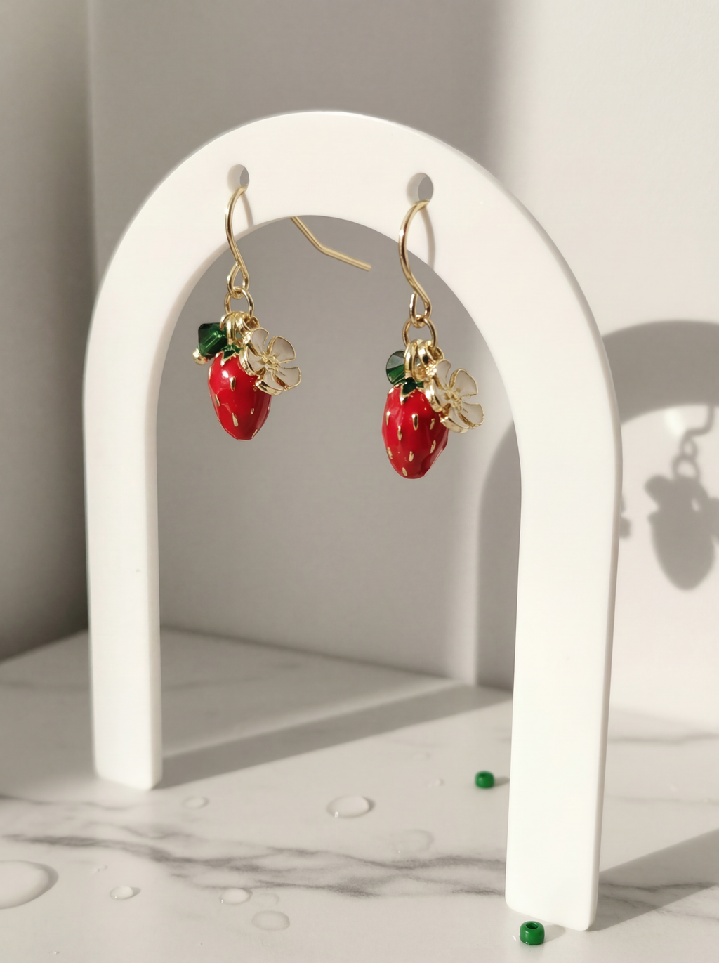 Strawberry-themed earrings on a white arch with a neutral background
