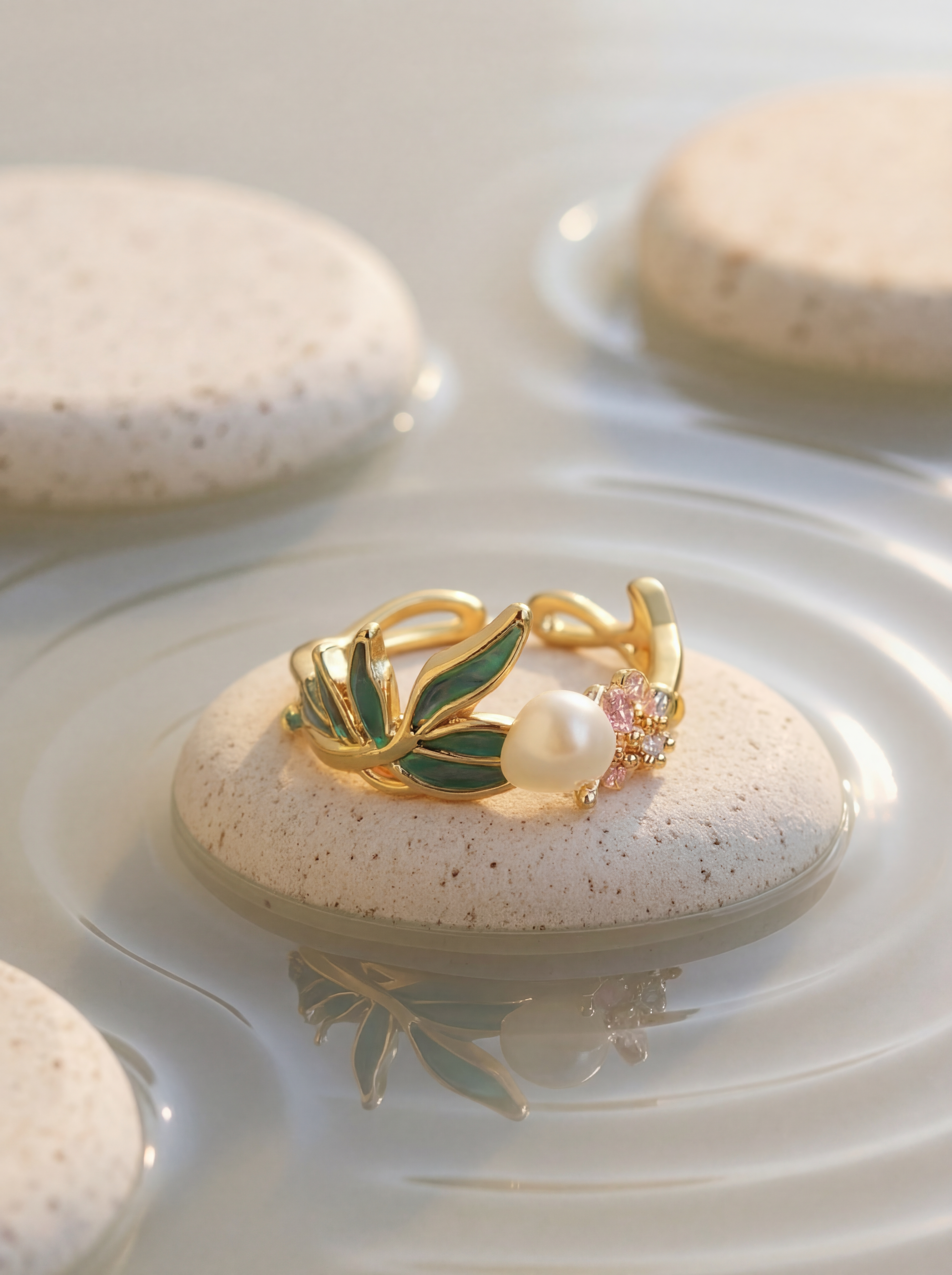 Gold ring with green leaf design and pearl on a stone with water