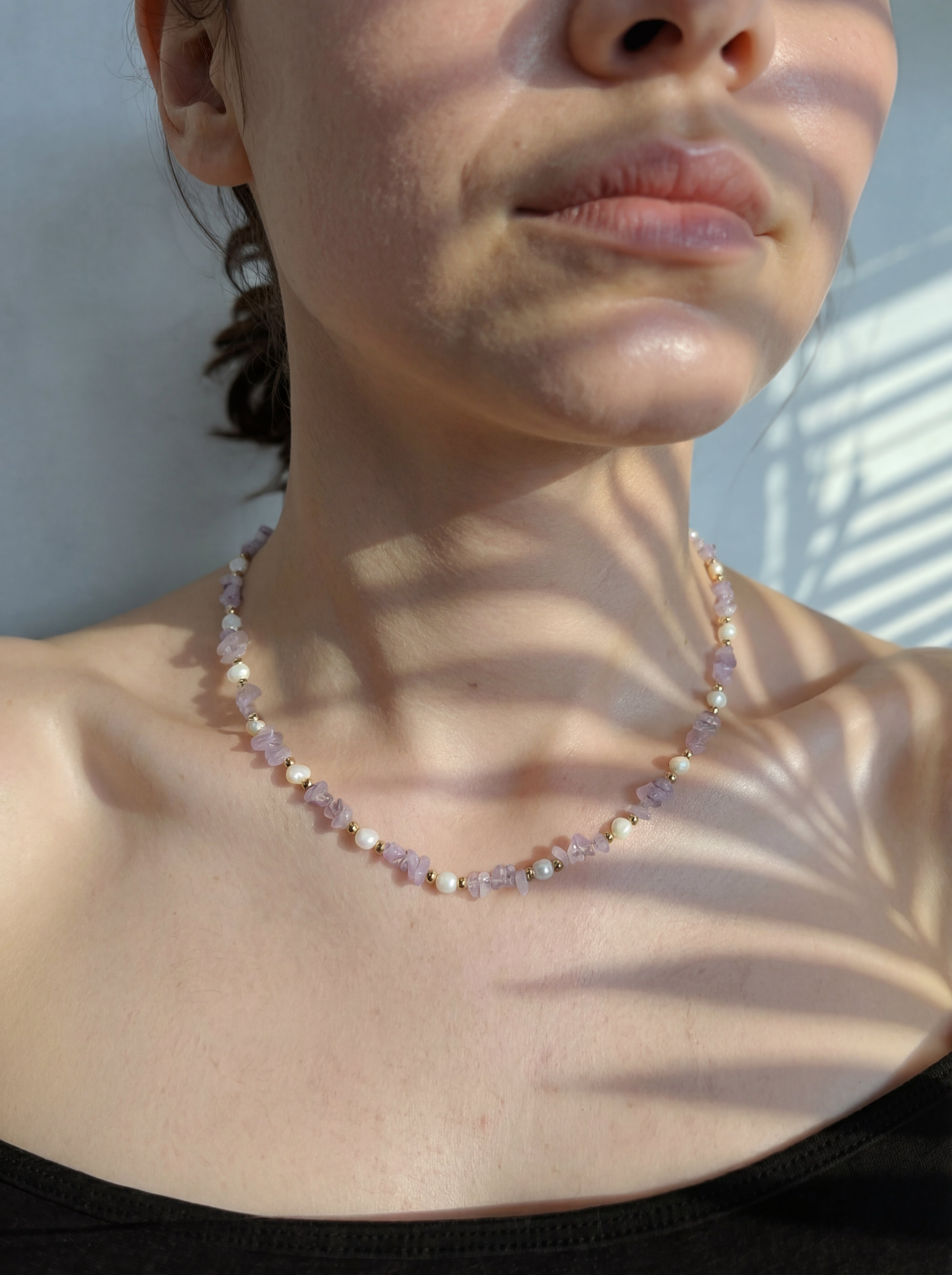 Close-up of a person wearing a beaded necklace with sunlight casting shadows.