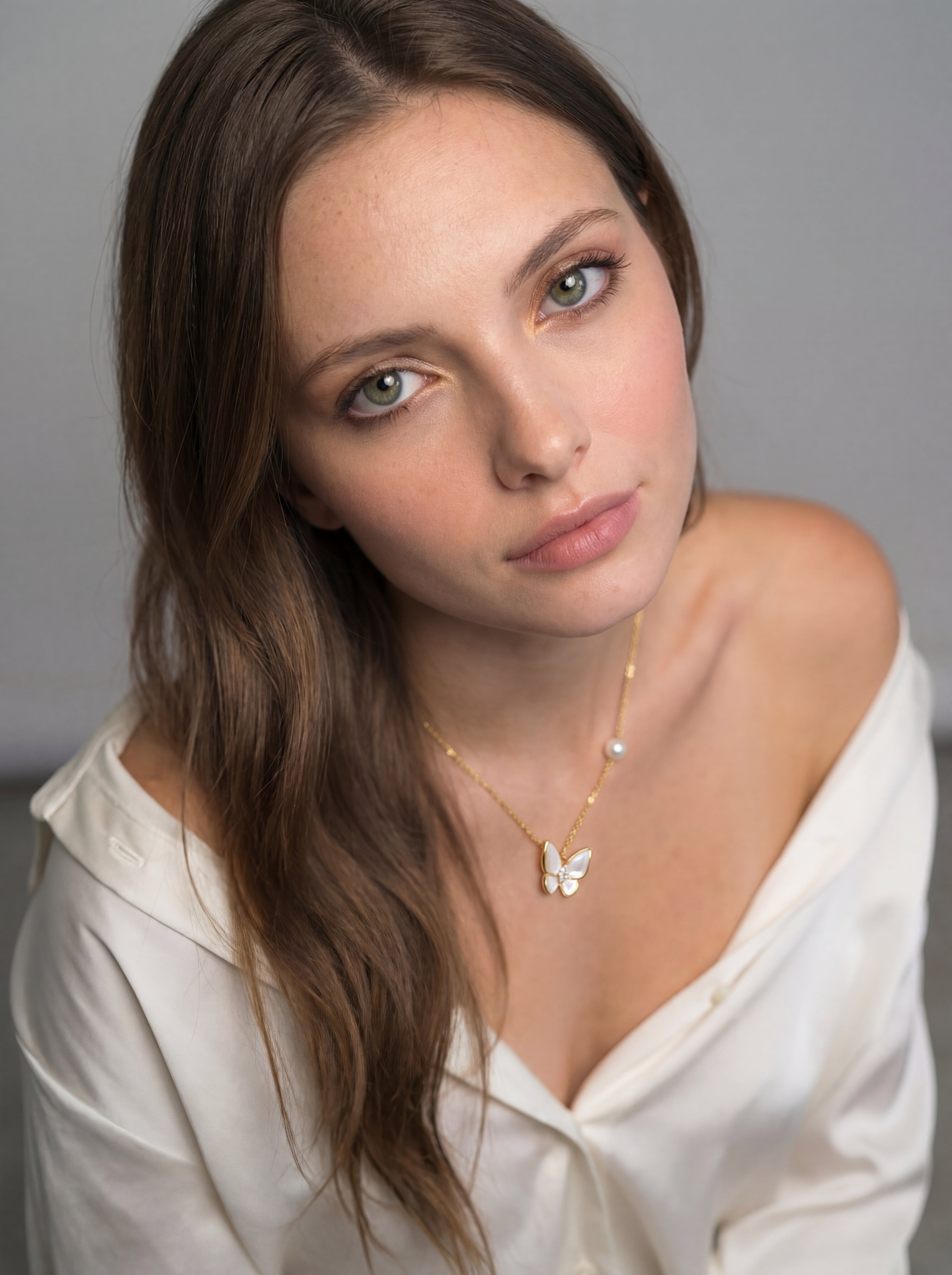 Woman wearing a white blouse and gold necklace with a butterfly pendant against a gray background