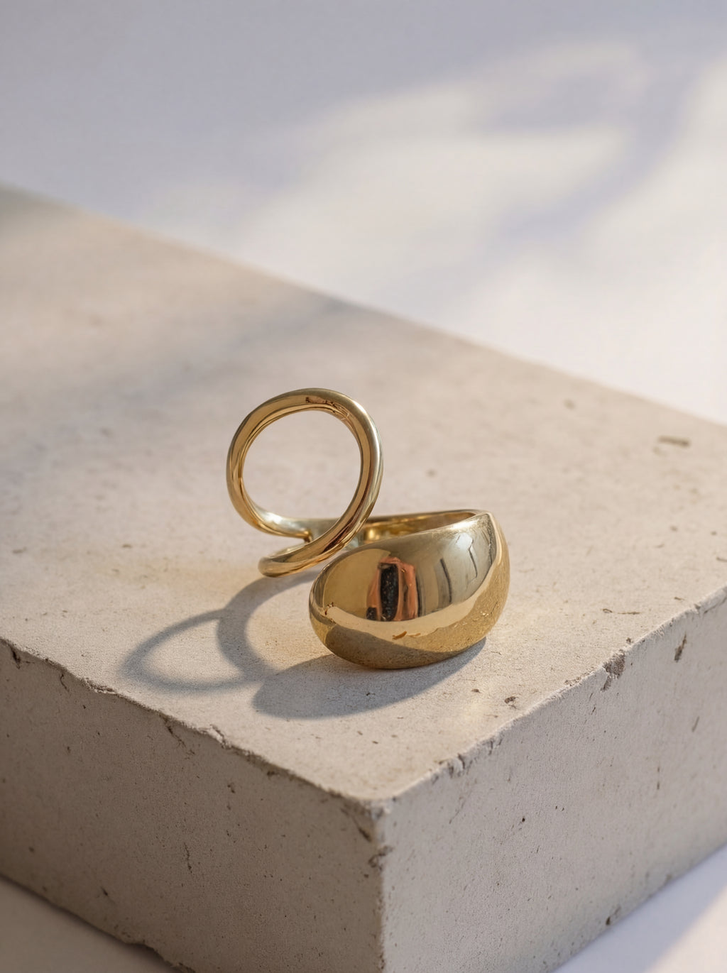 Gold ring on a light stone surface with soft shadows